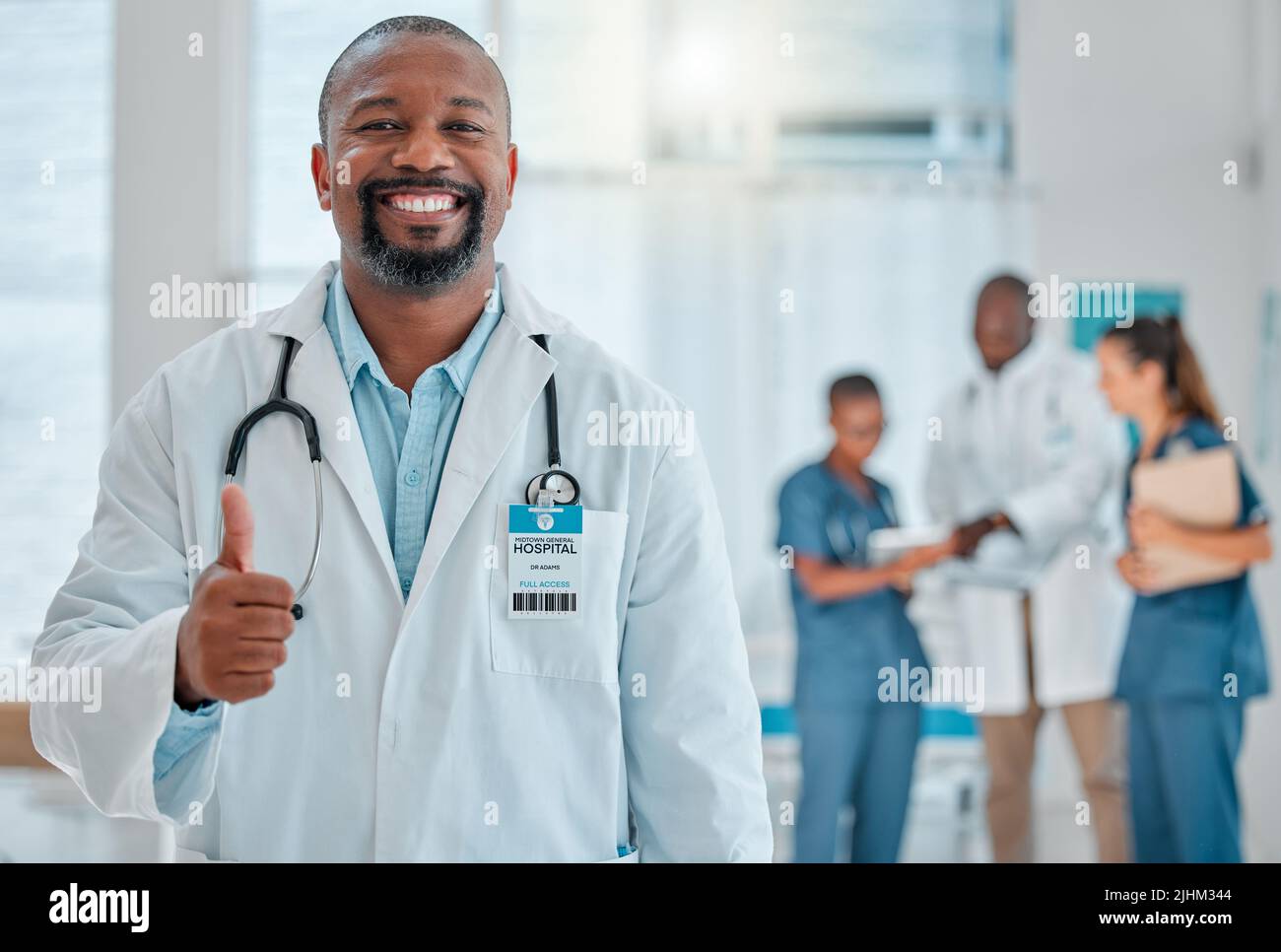Un médecin afro-américain mature montre un pouce en travaillant dans un hôpital avec des collègues. Professionnel de la santé expert souriant pendant la fabrication Banque D'Images
