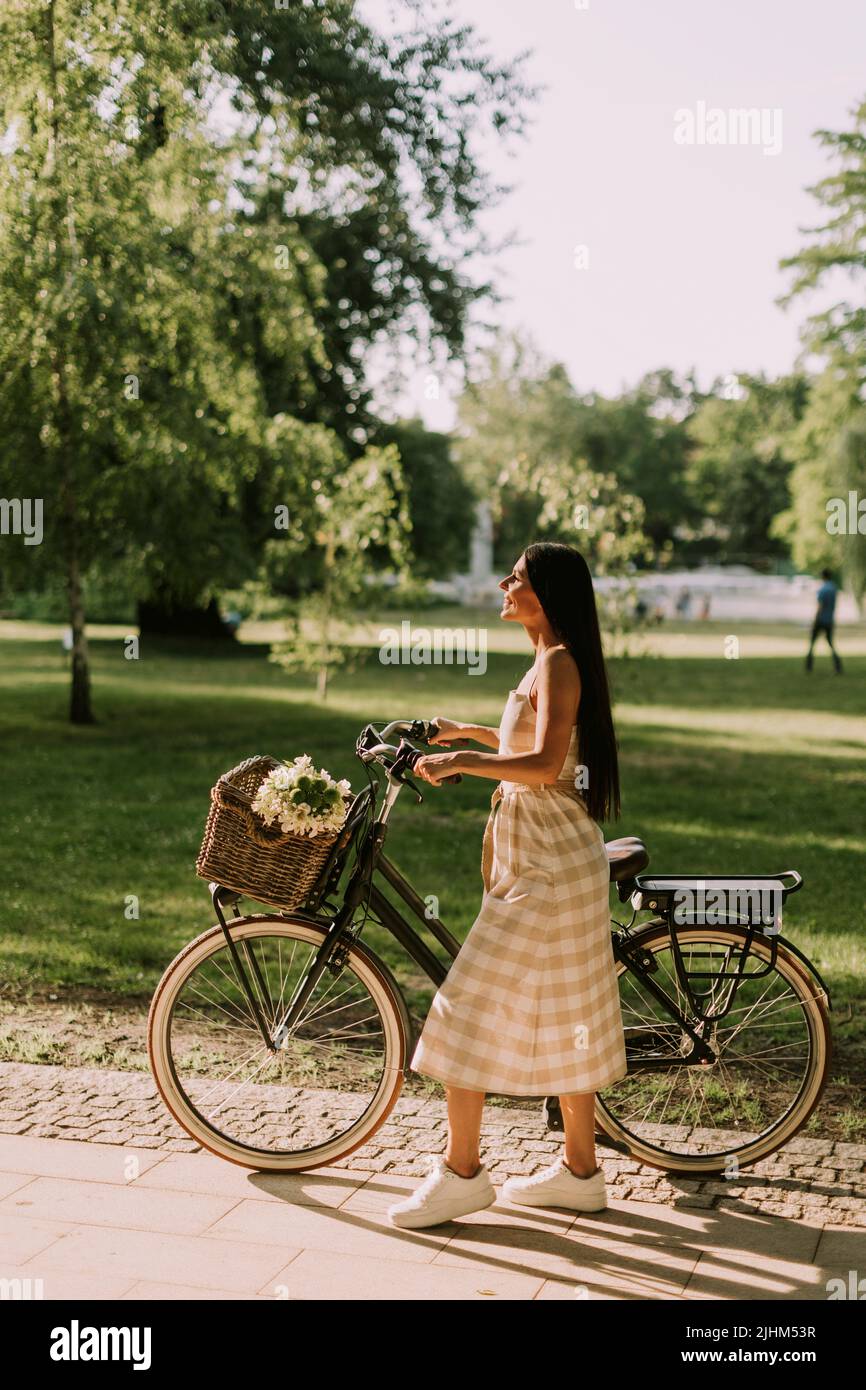 Jolie jeune femme avec des fleurs dans le panier de vélo électrique Banque D'Images