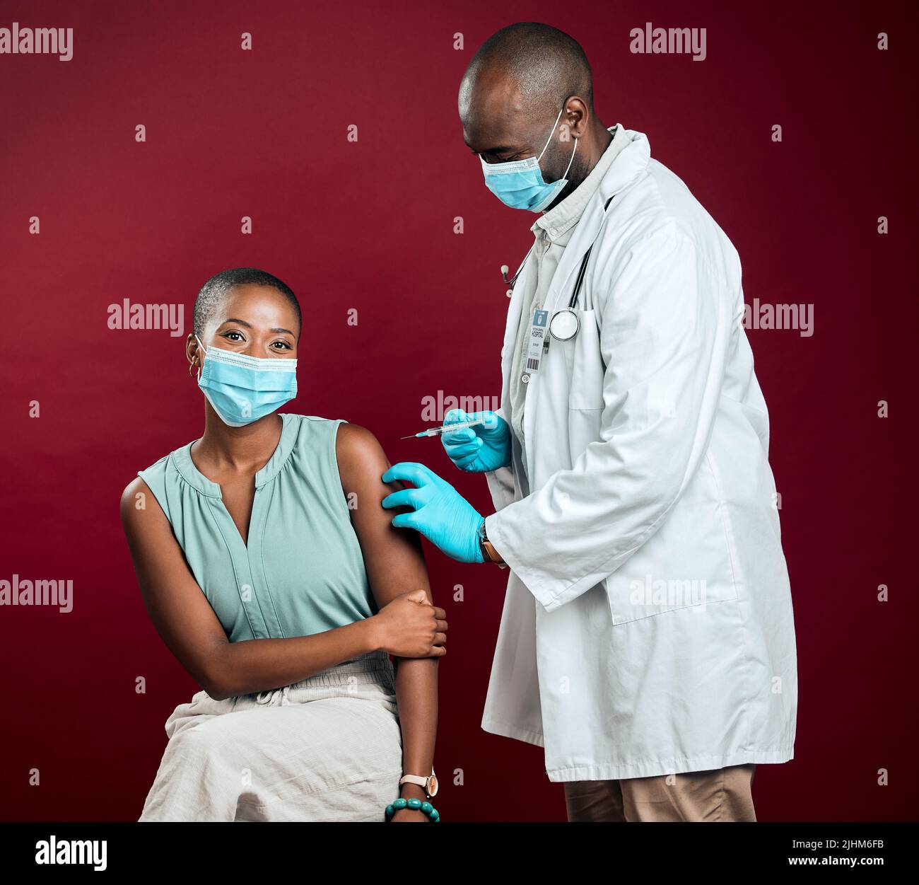 Un médecin afro-américain donne le vaccin contre le covid à une femme noire portant un masque chirurgical. Patient en bonne santé qui reçoit une injection de corona du médecin avec Banque D'Images