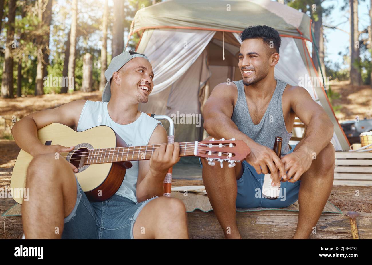 Laissez-moi vous chanter une chanson, bro. Un beau jeune homme assis avec son ami et jouant de la guitare dans les bois. Banque D'Images