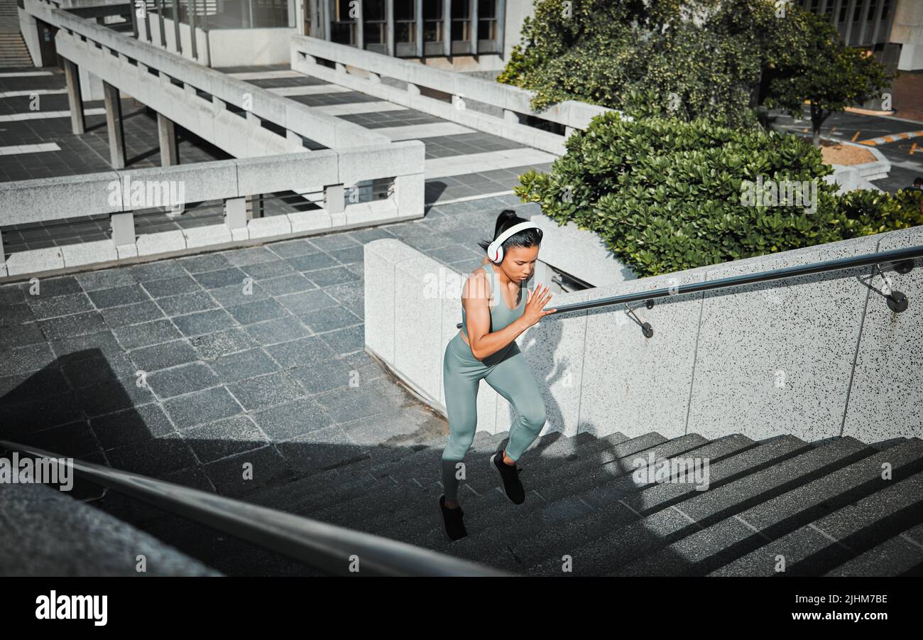 Jeune athlète féminine de course mixte portant des écouteurs à l'écoute de la musique et courant dans les escaliers à l'extérieur de la ville. L'exercice est bon pour votre santé et Banque D'Images