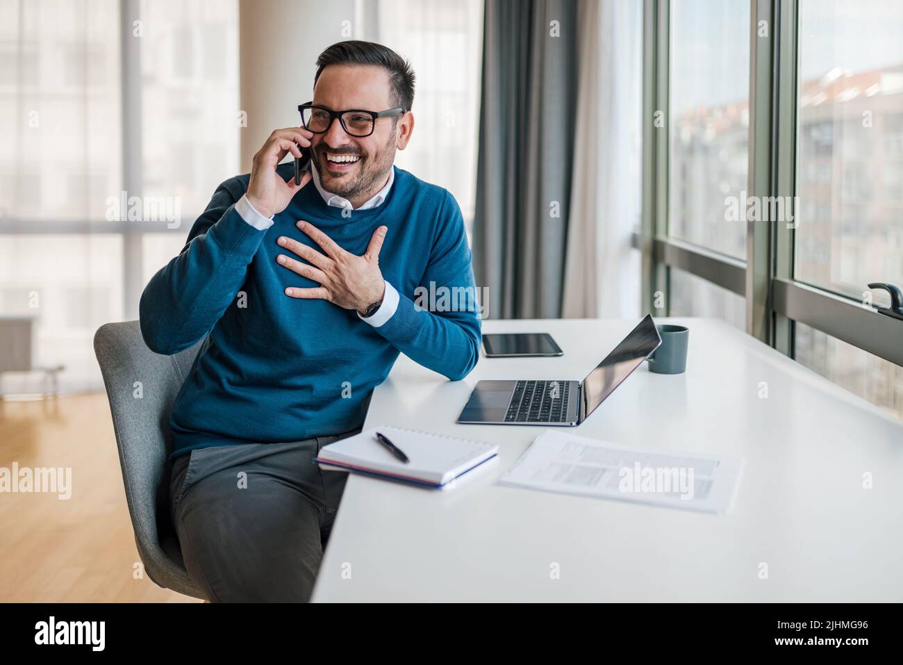 Heureux homme d'affaires du millénaire faisant appel au client, consultant le client, parlant sur smartphone devant l'ordinateur portable au bureau W Banque D'Images