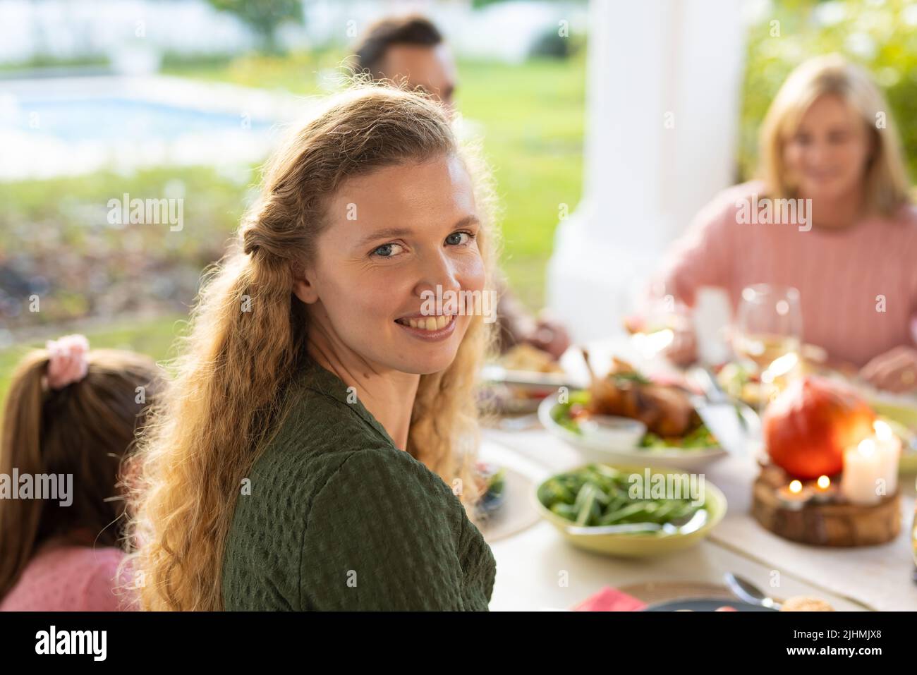 Image de la bonne femme caucasienne souriant à l'appareil photo et dînant en famille Banque D'Images