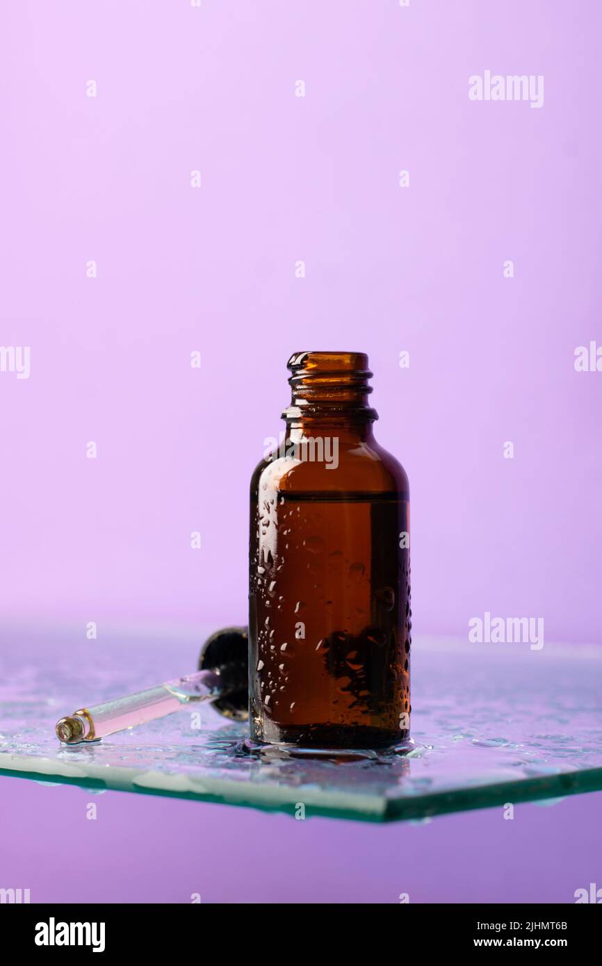 Bouteille de produit cosmétique, verre foncé avec pipette sur étagère en verre, fond violet, regarder vers le haut Banque D'Images