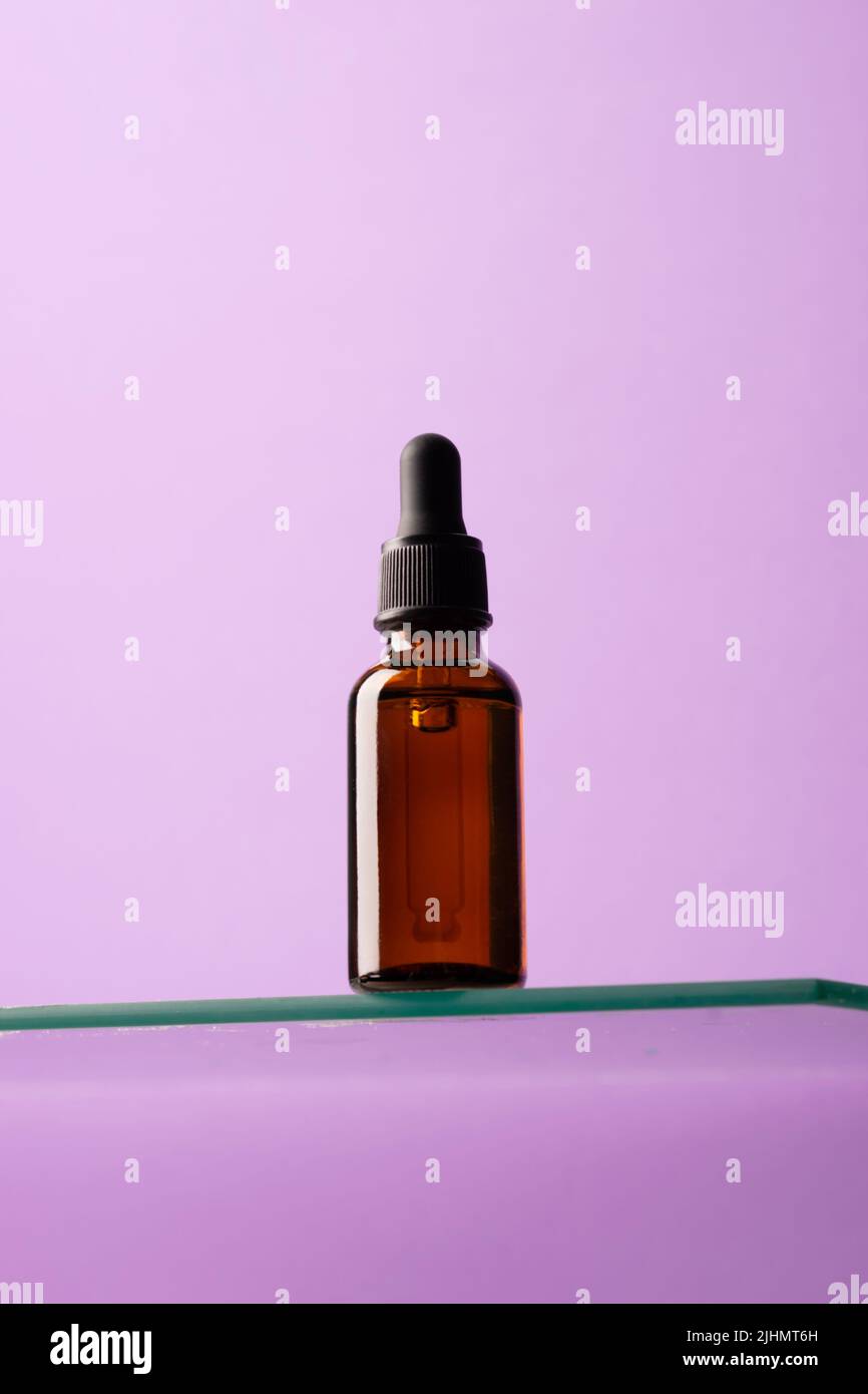 Bouteille de produit cosmétique, verre foncé avec pipette sur étagère en verre, fond violet, regarder vers le haut Banque D'Images