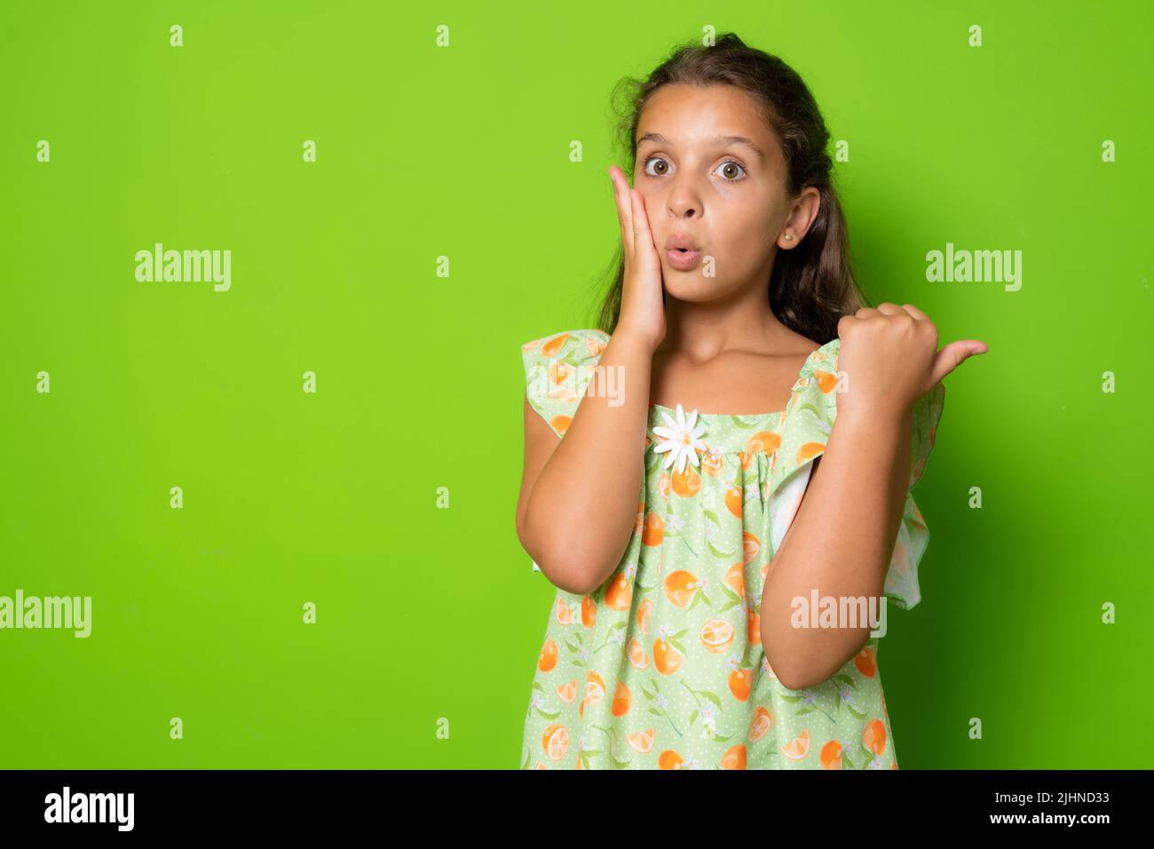 Choqué étonné mignon brunette petite fille enfant, toucher visage stupéfié, tourner pointant vers la droite copier l'espace stupéfié, la mâchoire de chute s'est demandé, stare speechless et aston Banque D'Images