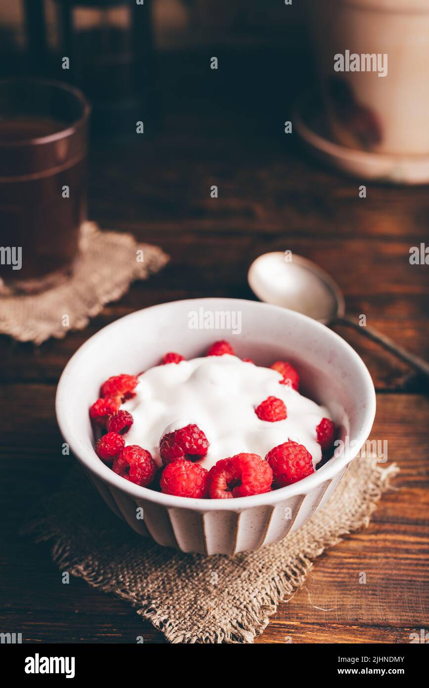 Bol de dessert d'été avec framboise et crème fraîche et verre de café sur une surface rustique Banque D'Images