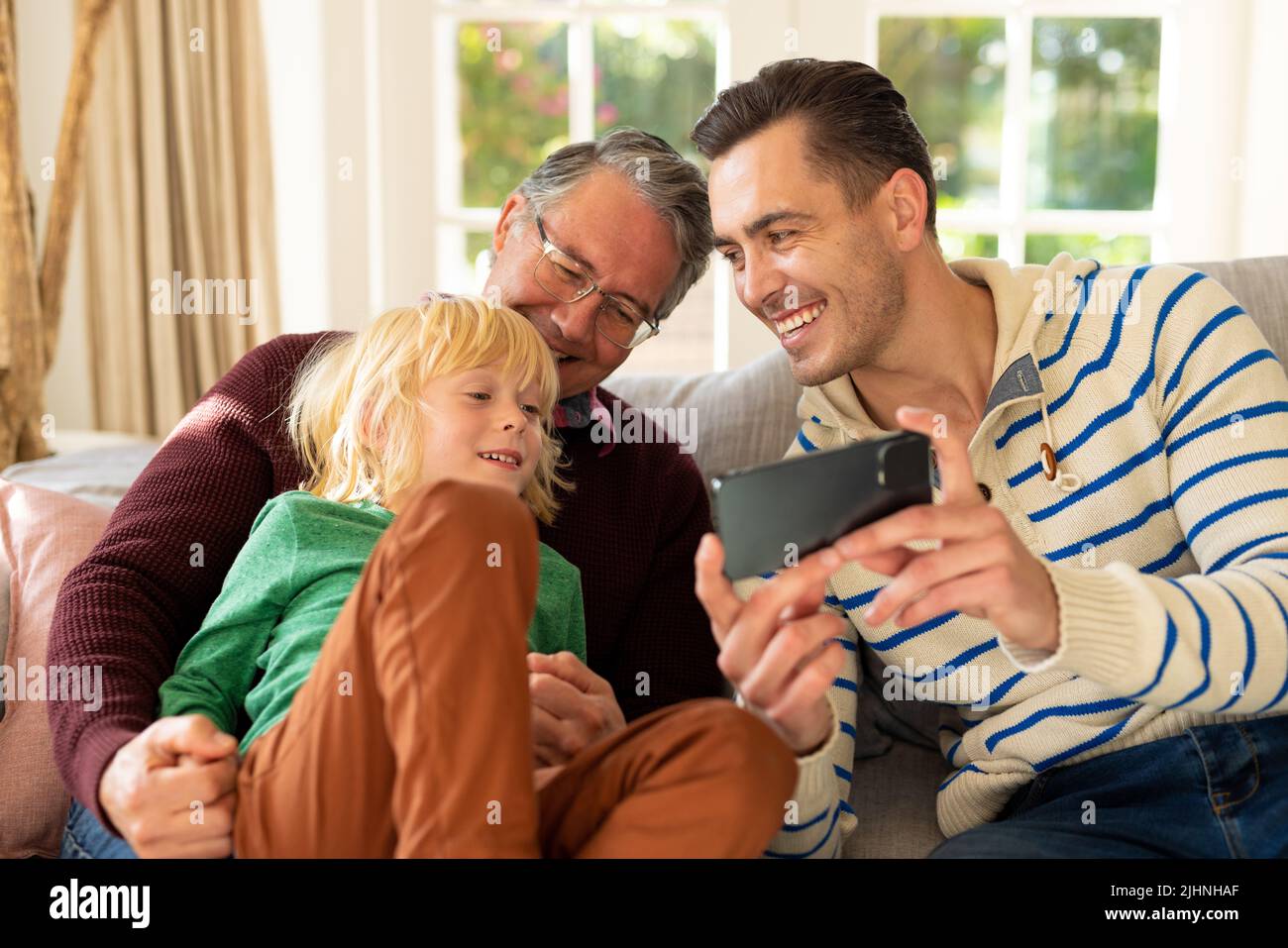 Image de trois générations d'hommes caucasiens heureux assis sur un canapé et en utilisant un smartphone Banque D'Images