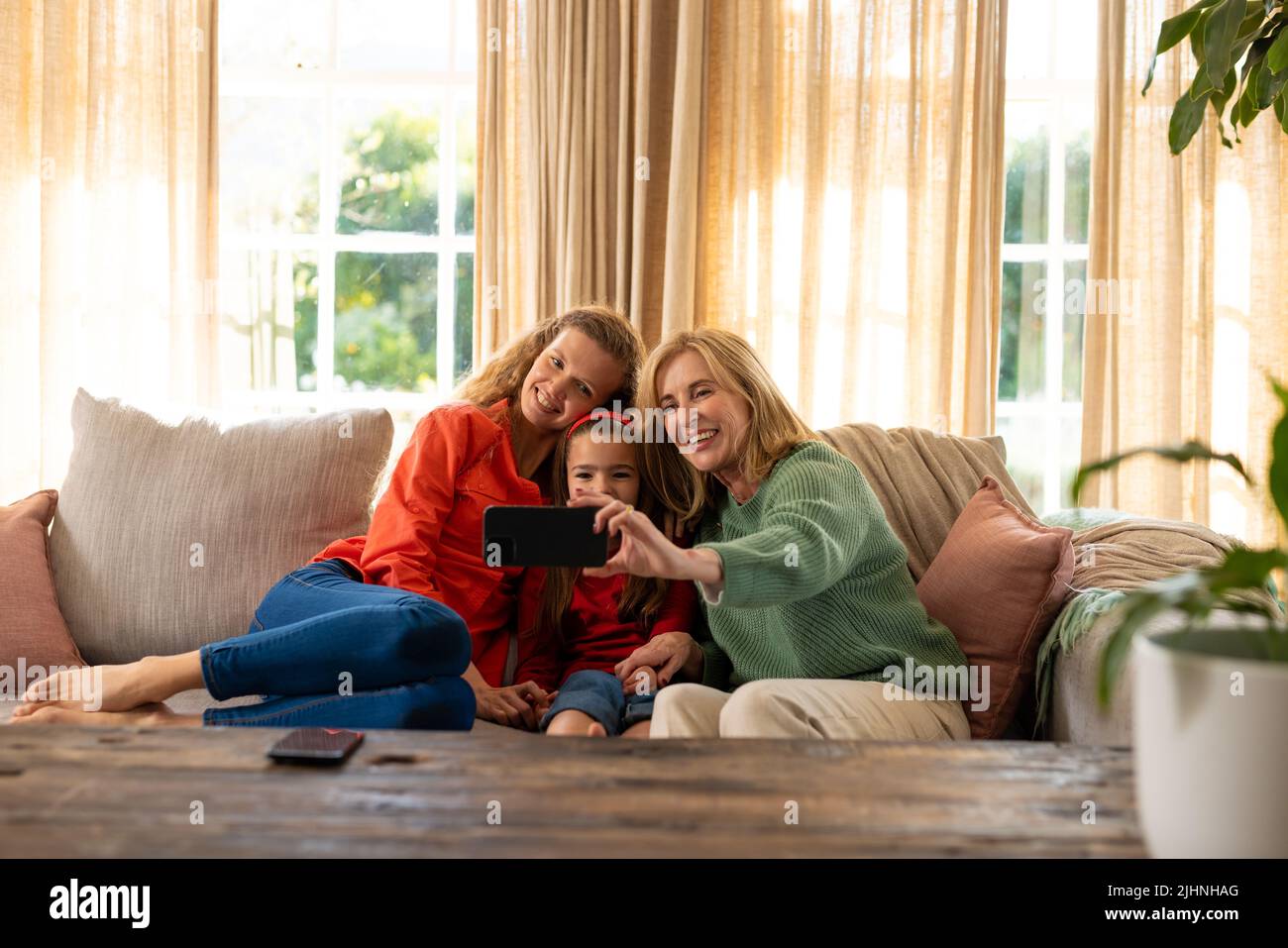 Image de femmes caucasiennes de trois générations heureuses assises sur un canapé et prenant le selfie Banque D'Images