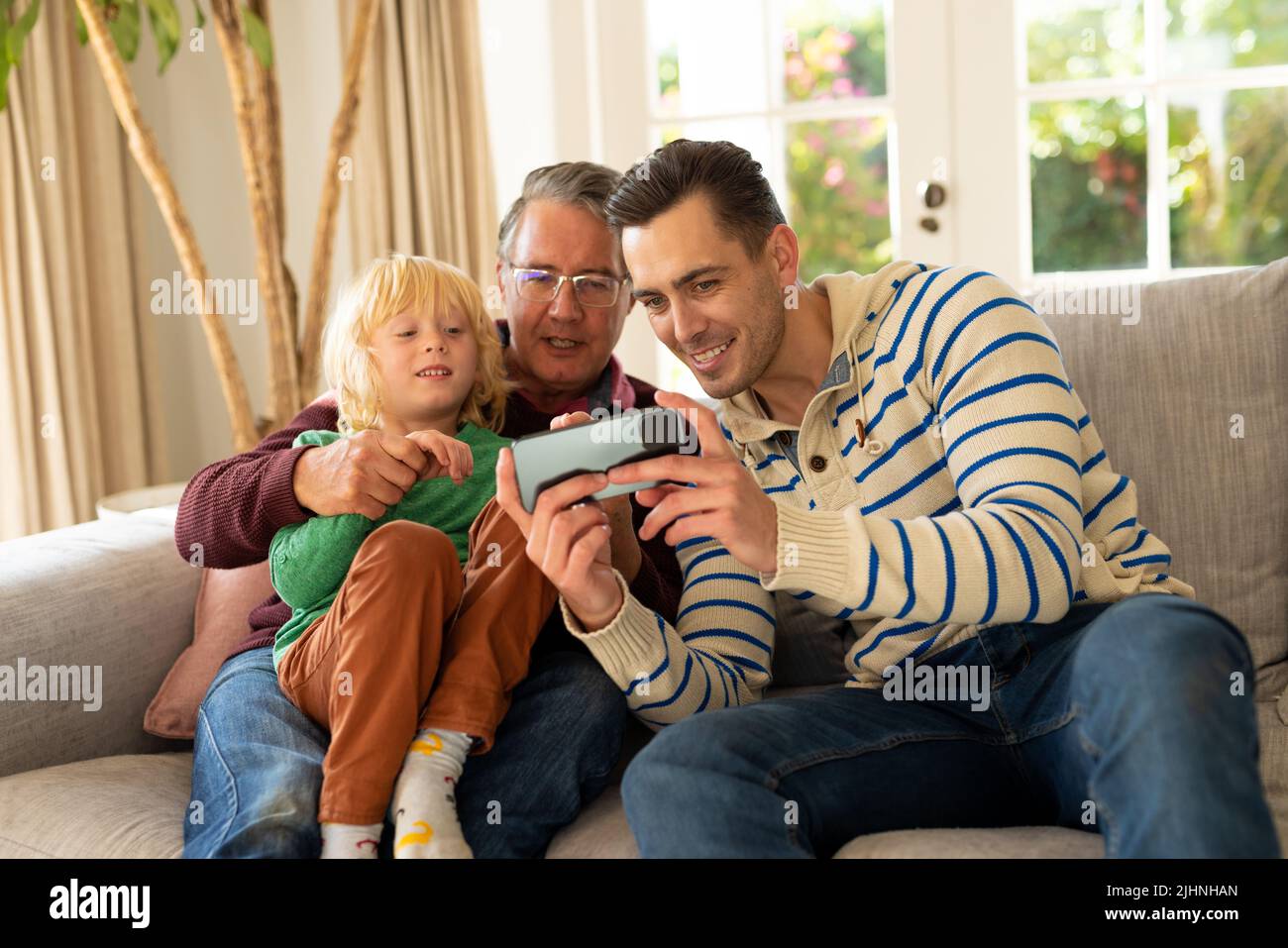 Image de trois générations d'hommes caucasiens heureux assis sur un canapé et en utilisant un smartphone Banque D'Images