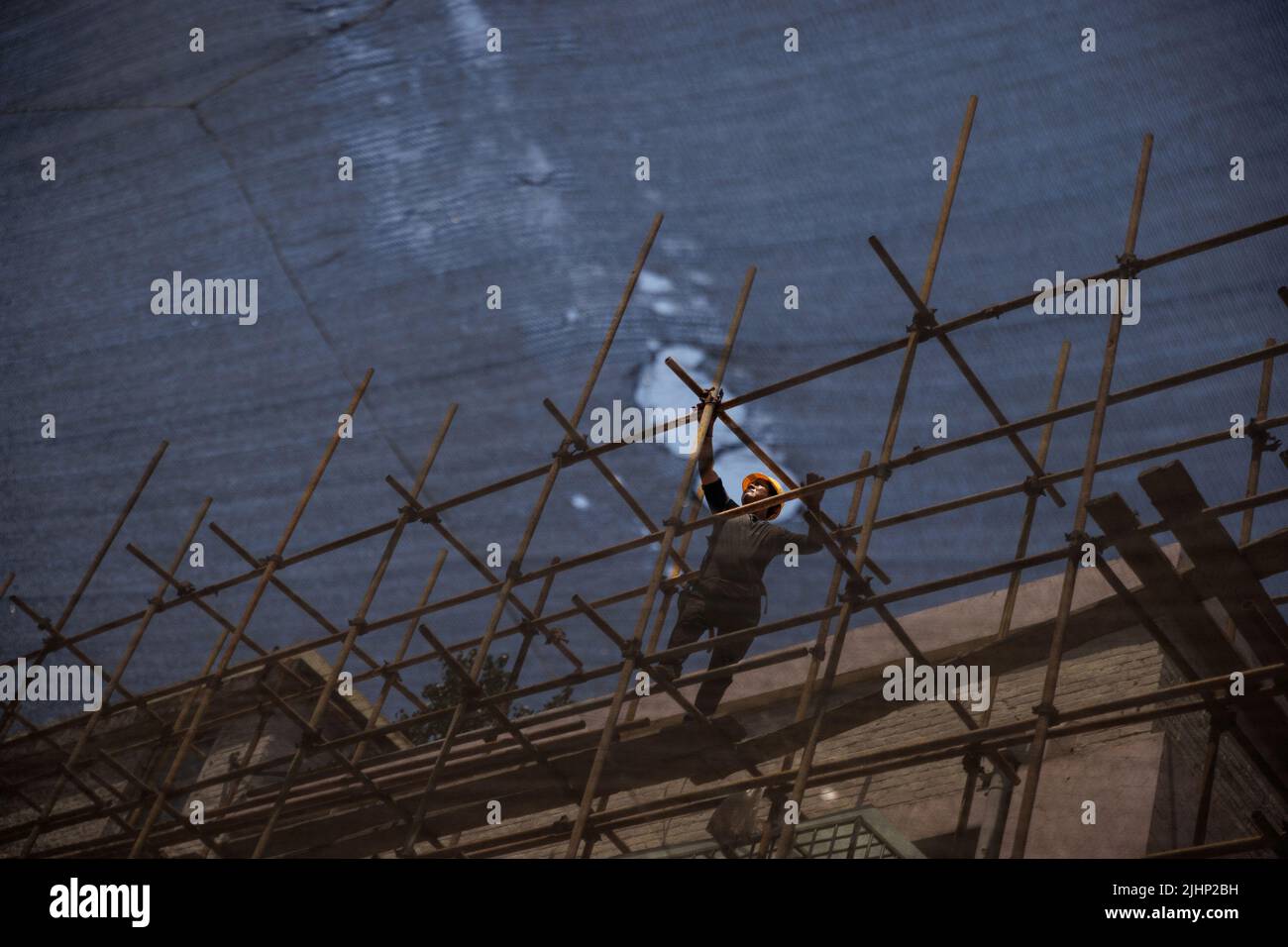 Un travailleur est vu à travers un filet de protection lorsqu'il serre un échafaudage sur un site de construction d'un immeuble en cours de rénovation à Beijing, en Chine, au 20 juillet 2022. REUTERS/Thomas Peter Banque D'Images