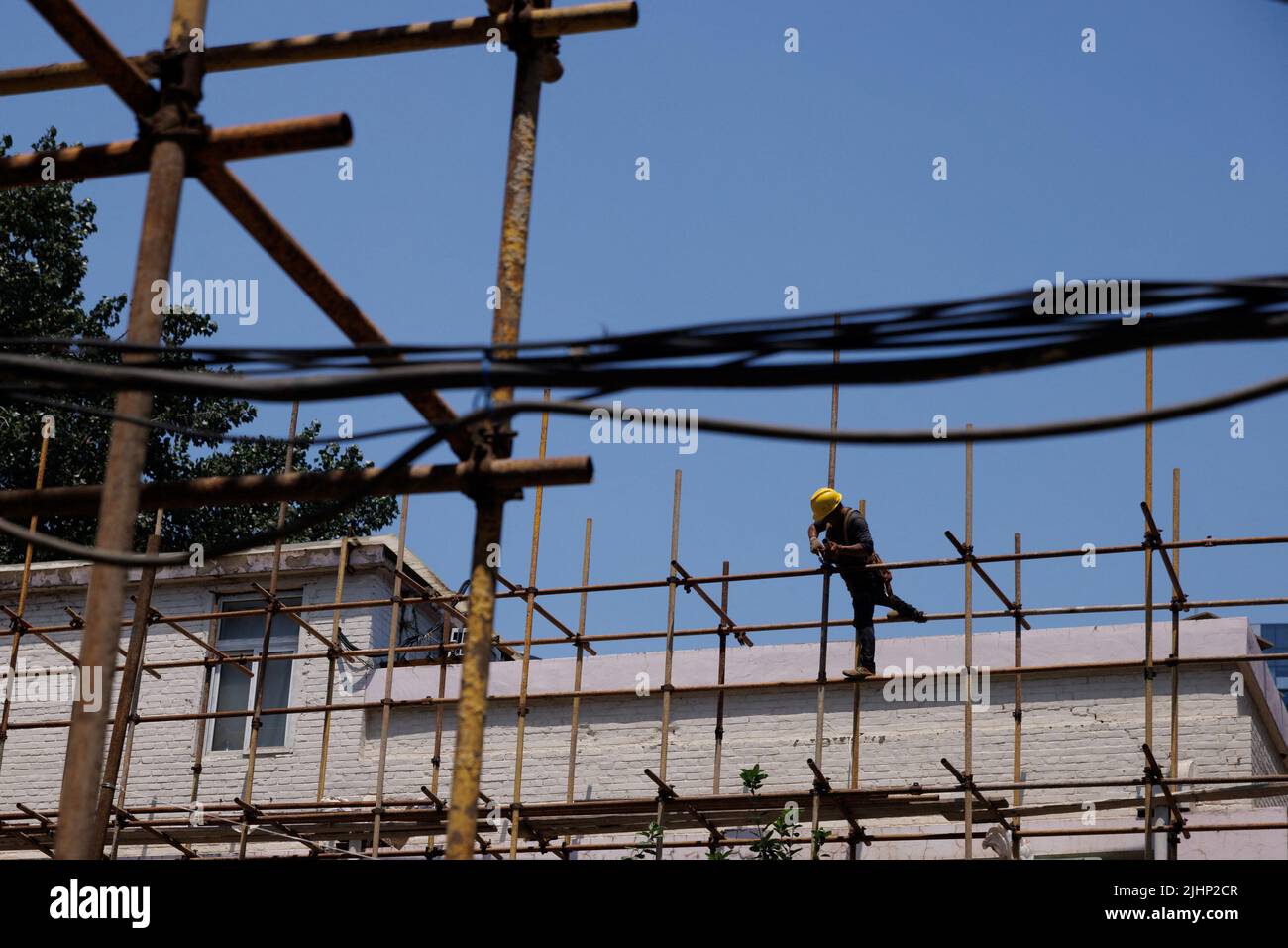 Un ouvrier serre un échafaudage sur un chantier de construction d'un immeuble en cours de rénovation à Pékin, en Chine, au 20 juillet 2022. REUTERS/Thomas Peter Banque D'Images