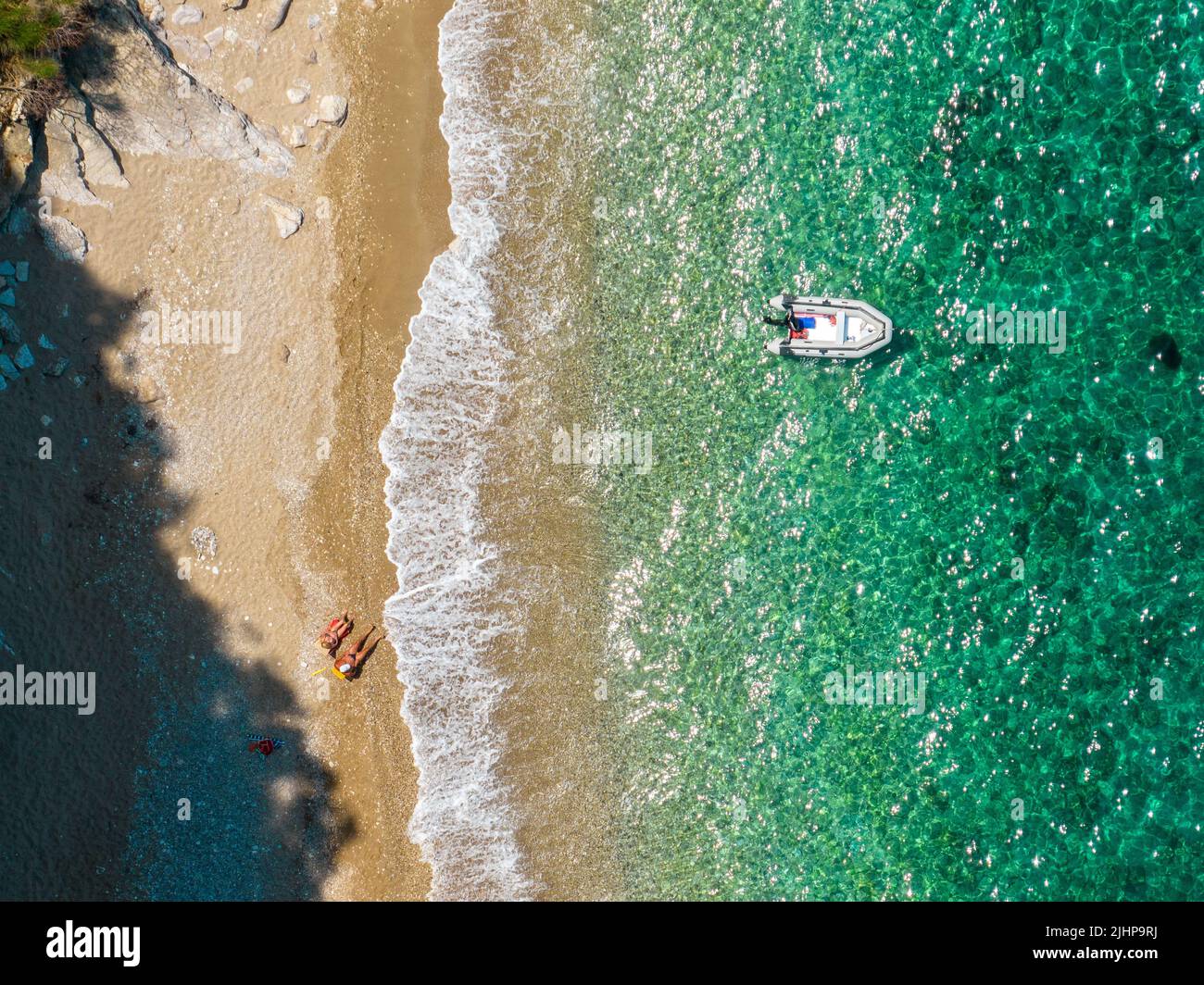 Vue aérienne d'un canot amarré flottant sur une mer transparente. La plage et les personnes assises et relaxantes. Côte, Corfou, Grèce Banque D'Images