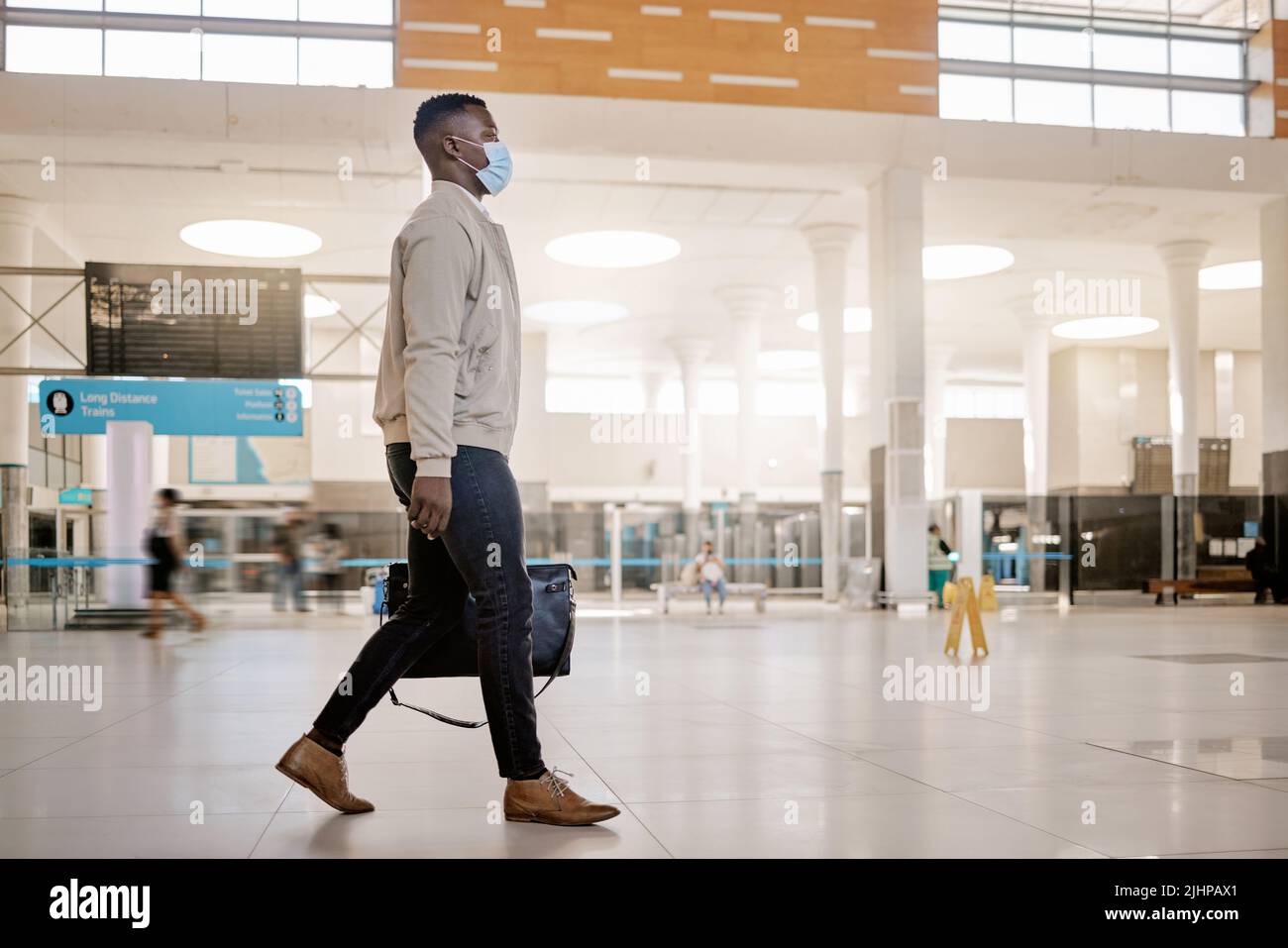 Homme d'affaires afro-américain voyageant seul et marchant dans une gare tout en portant un masque de protection contre le coronavirus. Jeune homme noir Banque D'Images