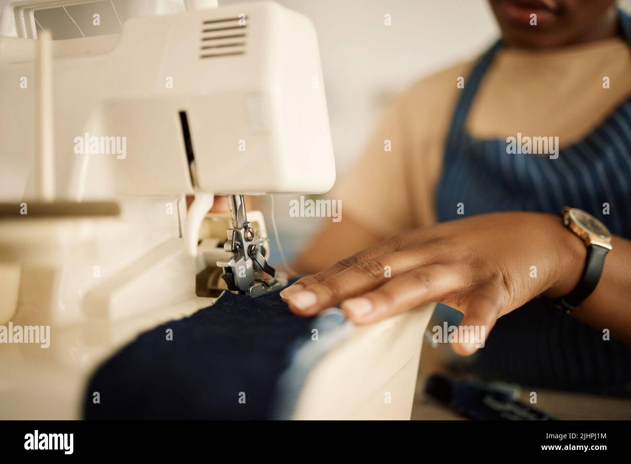 Gros plan des mains de tailleur à l'aide d'une machine à coudre. Couturier alimentant le denim à travers la machine à coudre. Main d'une couturière couture d'un morceau de Banque D'Images