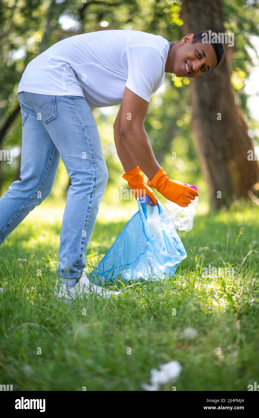 Un gars souriant à la caméra se pencher pour ramasser les déchets Banque D'Images