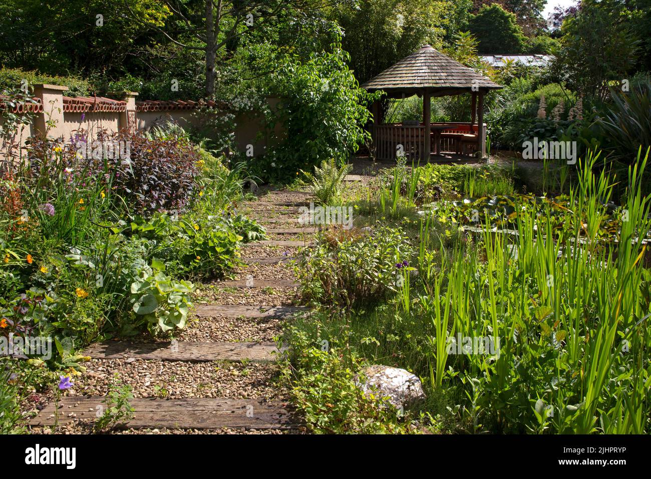 Jardin anglais avec étang ornemental avec élément de maison d'été et chemin de gravier avec des dormeuses en bois, Angleterre Banque D'Images