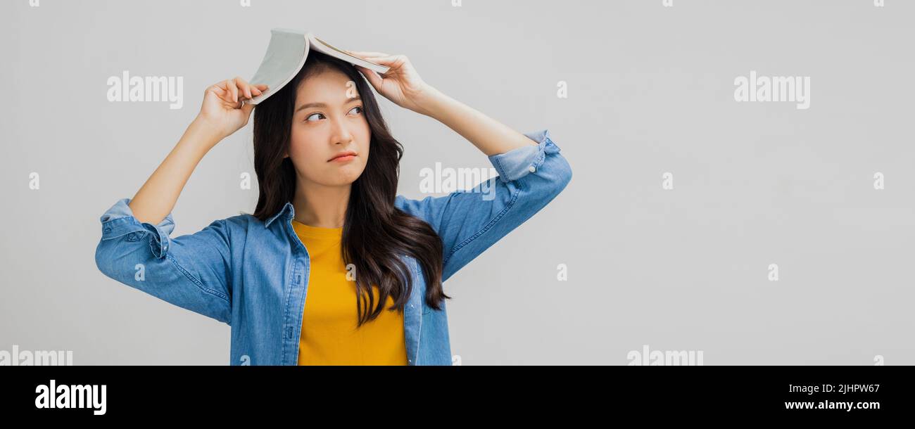 Belle femme asiatique ennuyeux et tenant le livre sur sa tête, fatigué et ennuyé jeune fille étudiante Banque D'Images