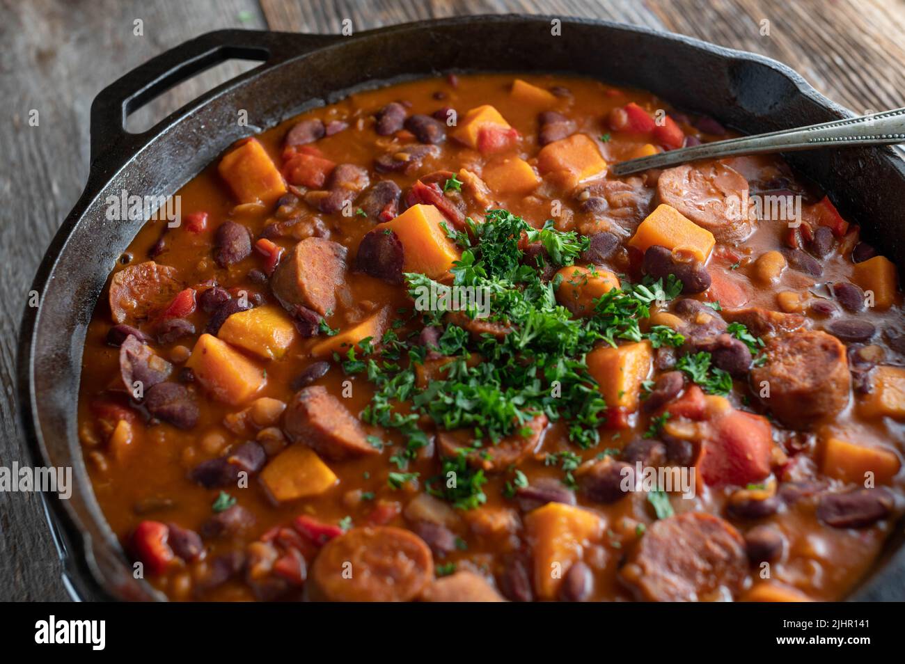 Ragoût de haricots mexicains avec chorizo salami, patates douces et légumes dans une casserole en fonte isolée sur une table en bois Banque D'Images