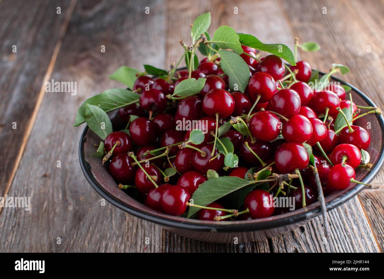 Bol avec des cerises aigres fraîchement cueillies. Servi dans un bol en émail brun isolé sur une table en bois avec espace de copie Banque D'Images