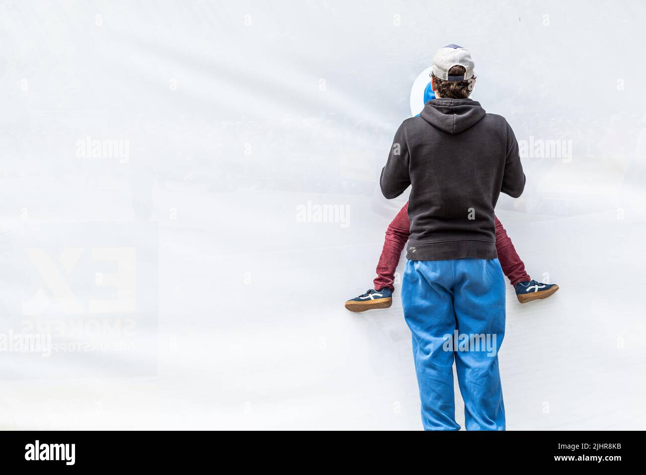 Homme portant un enfant afin que ce dernier puisse observer une scène à travers une toile blanche percée d'un trou d'observation. Banque D'Images