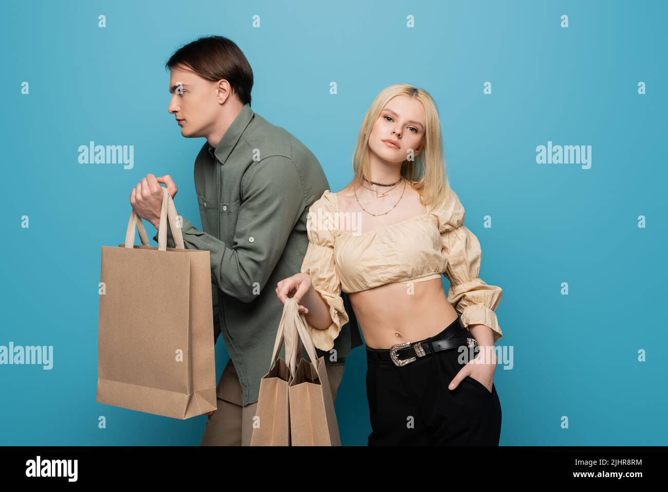 Une jeune femme en chemisier pose avec des sacs de shopping près d'un petit ami sur fond bleu Banque D'Images