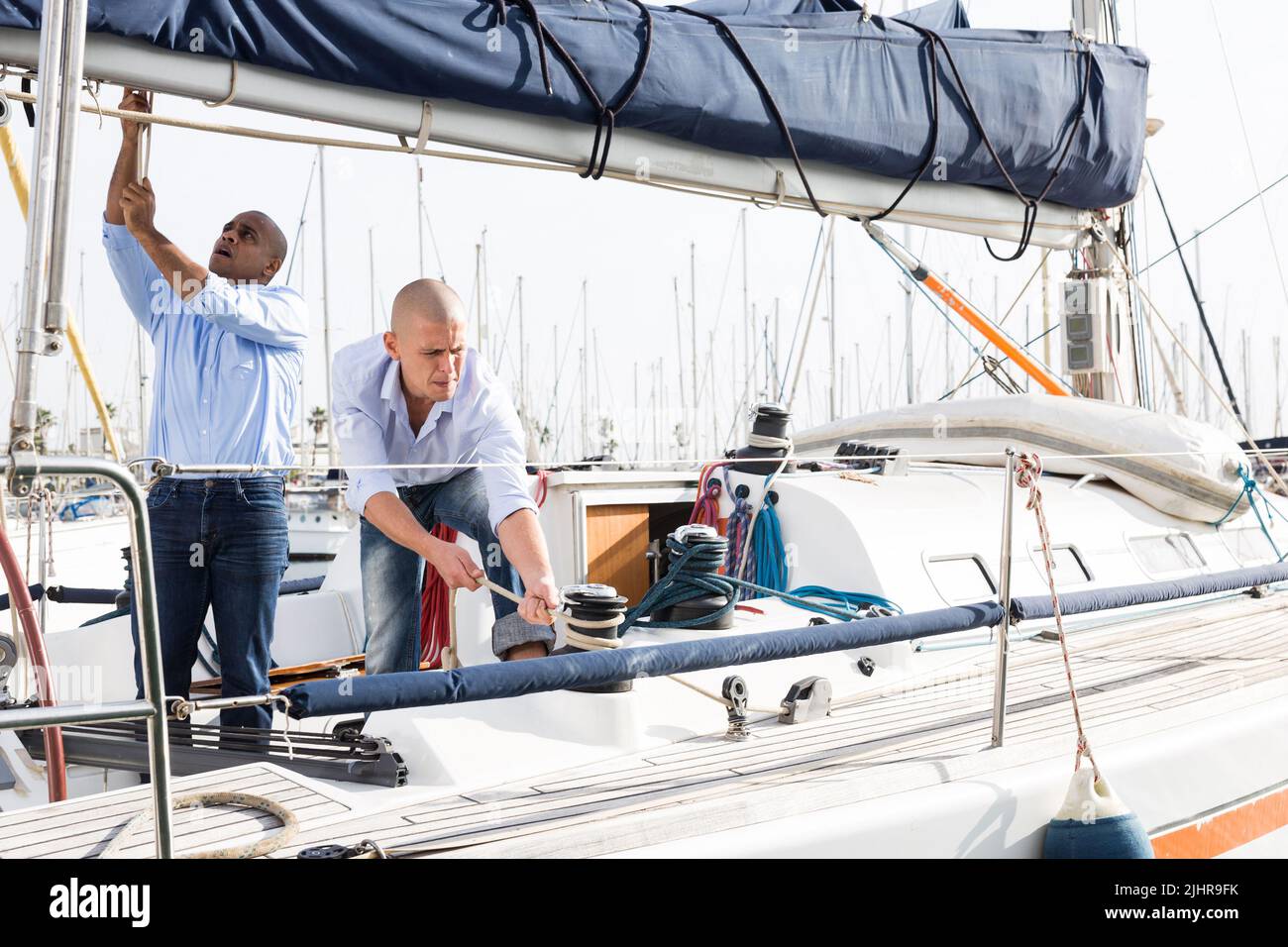 Deux jeunes hommes en chemises bleues arrange le yacht privé de voile dans le port maritime Banque D'Images