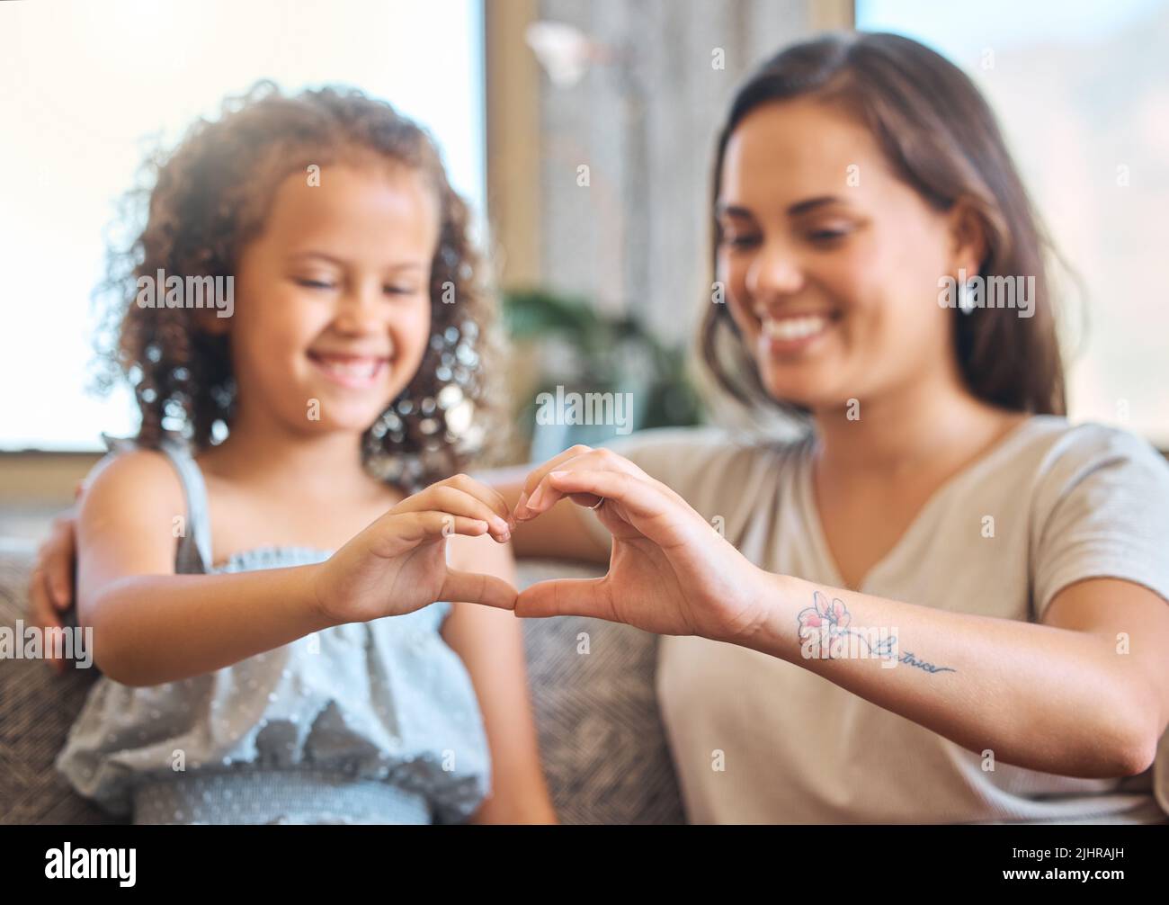 Famille aimante avec une mère célibataire et une adorable fille assise ensemble et formant une forme de coeur avec leurs mains sur le canapé à la maison. Doux Banque D'Images