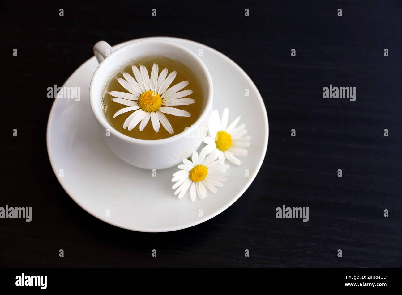 Thé de camomille dans une tasse blanche, fleurs de Marguerite sur la soucoupe. Boisson aux plantes médicinales sur une table en bois sombre Banque D'Images