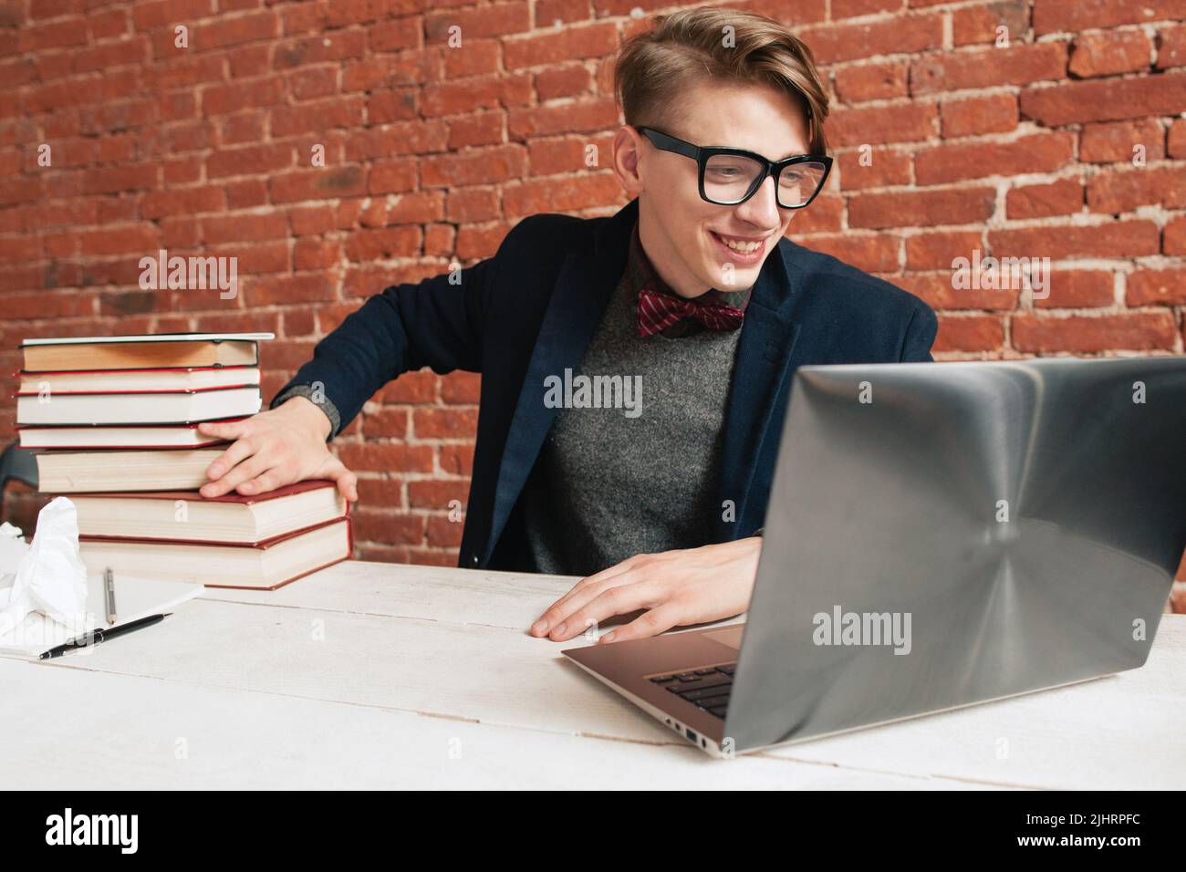 Homme souriant avec ordinateur portable, éloignez-vous d'une pile de livres Banque D'Images