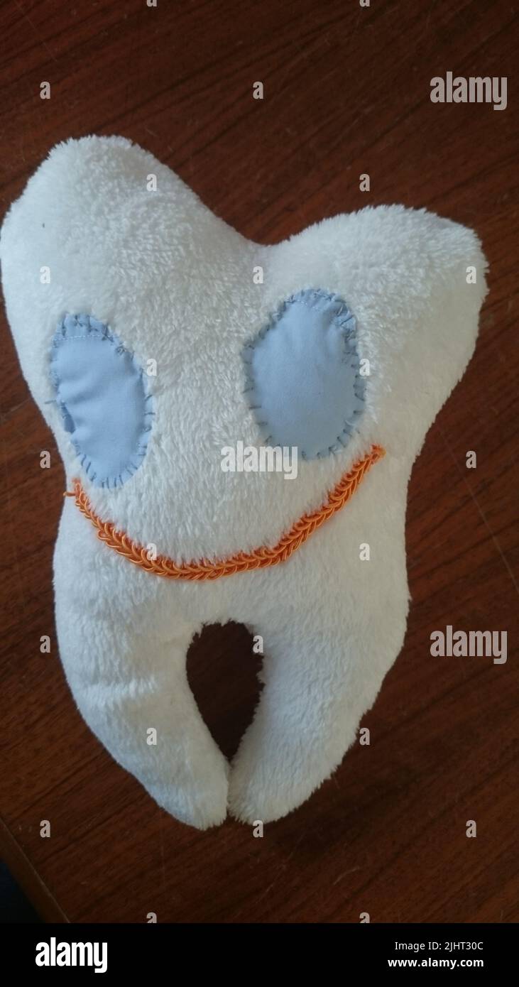 Une dent blanche en peluche cousue à la main avec des yeux bleus et une bouche souriante Banque D'Images