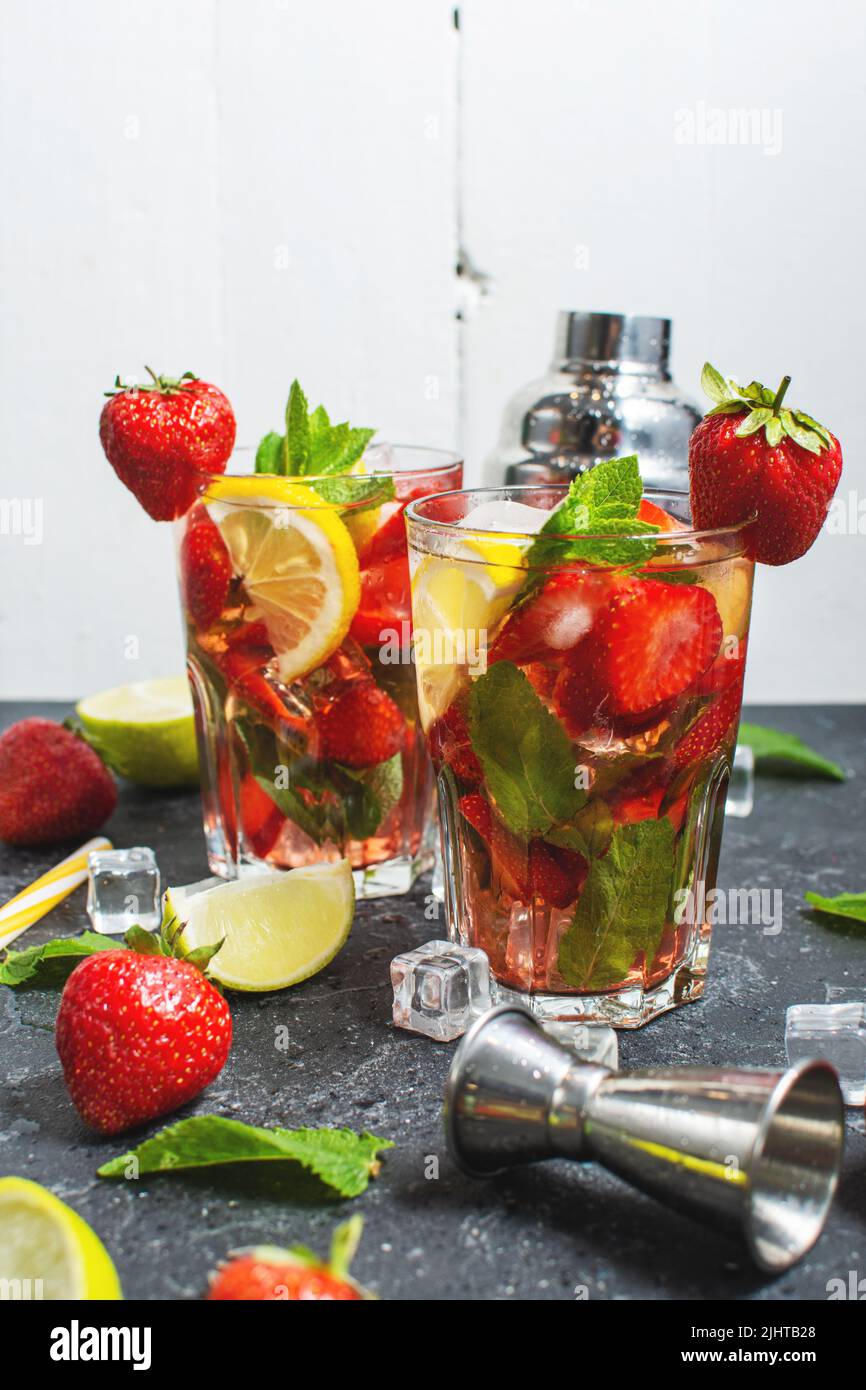 Cocktail de mojito rafraîchissant d'été avec fraise, menthe et citron vert avec shaker pour fouetter des boissons sur une table en pierre sombre Banque D'Images