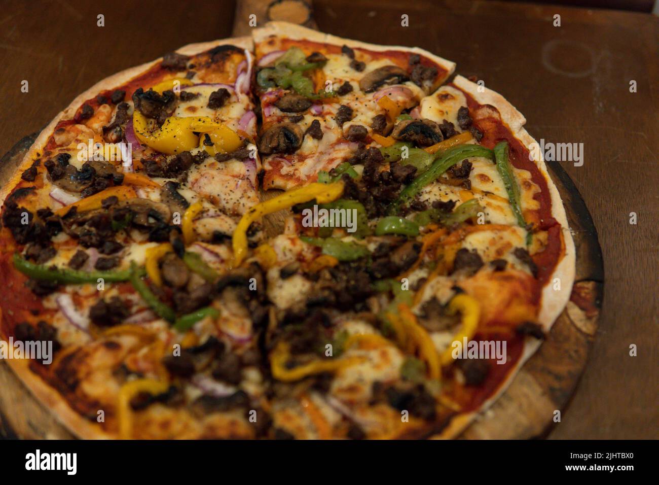 Pizza aux champignons avec de la viande et des poivrons fraîchement cuits sur une planche en bois et une table en bois servie pour le client. Table faite dans un four à bois servi à un r Banque D'Images