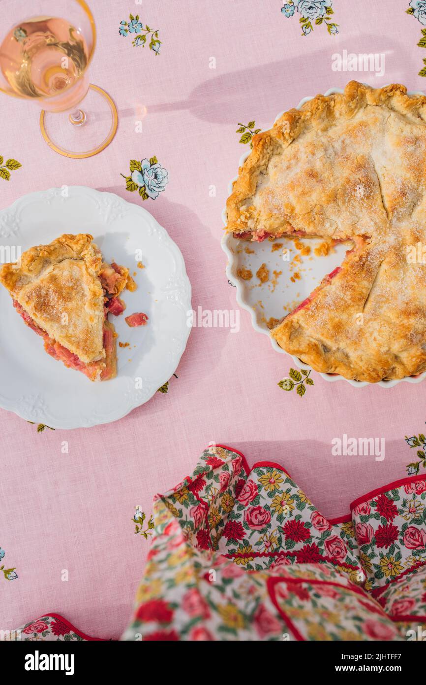 une seule tranche de tarte à la rhubarbe sur plaque blanche, nappe rose avec roses bleues Banque D'Images