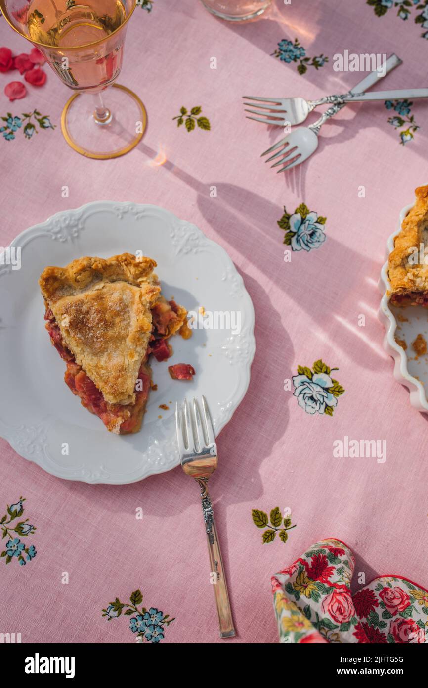 une seule tranche de tarte à la rhubarbe sur plaque blanche, nappe rose avec roses bleues Banque D'Images
