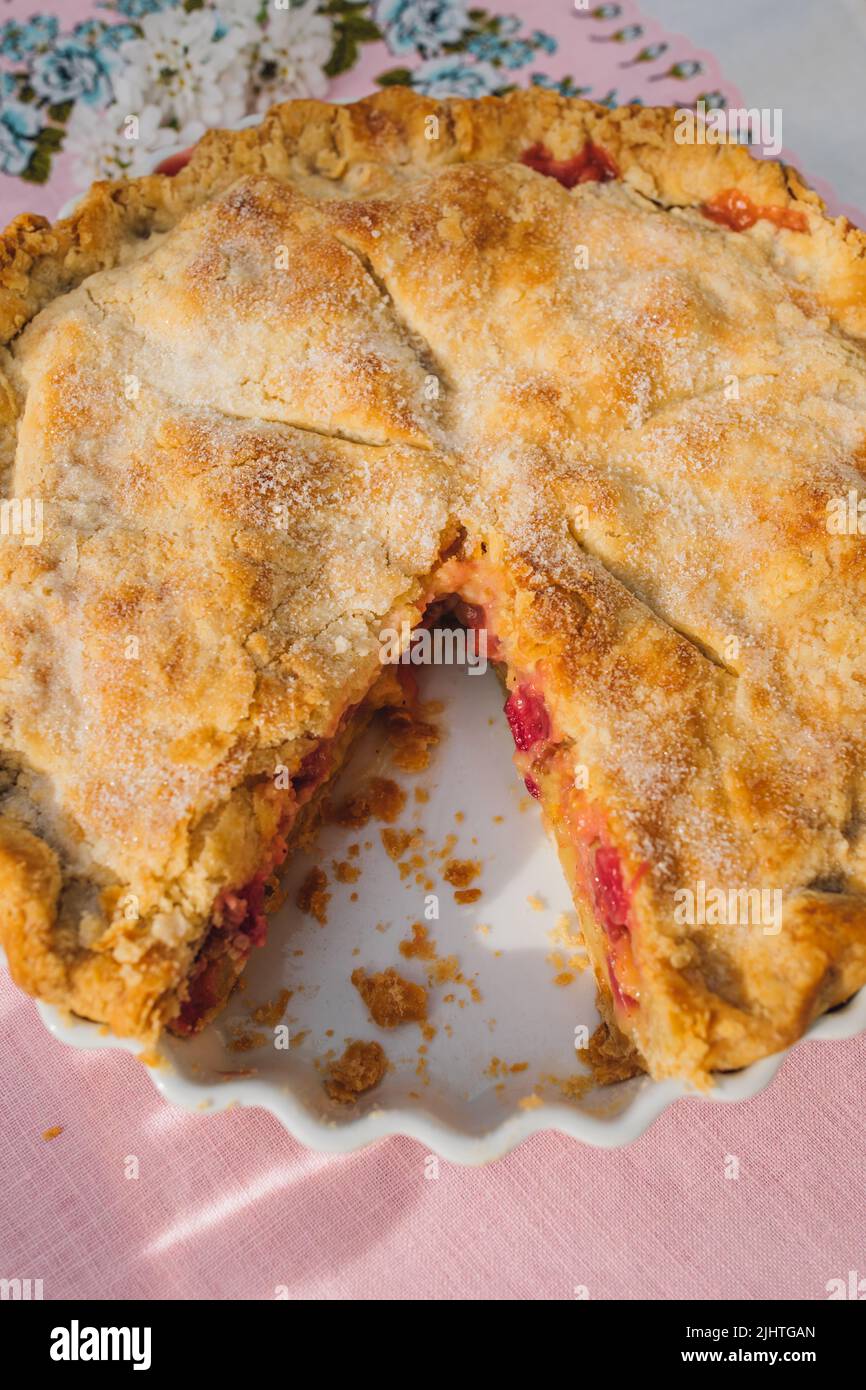 vue de haut en bas de la tarte à la rhubarbe avec tranche manquante, nappe rose avec roses bleues Banque D'Images