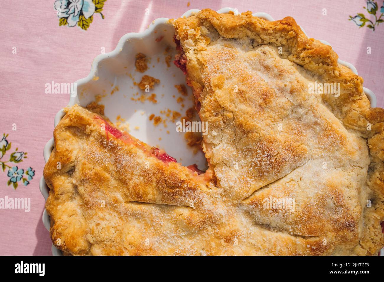 vue de haut en bas de la tarte à la rhubarbe avec tranche manquante, nappe rose avec roses bleues Banque D'Images