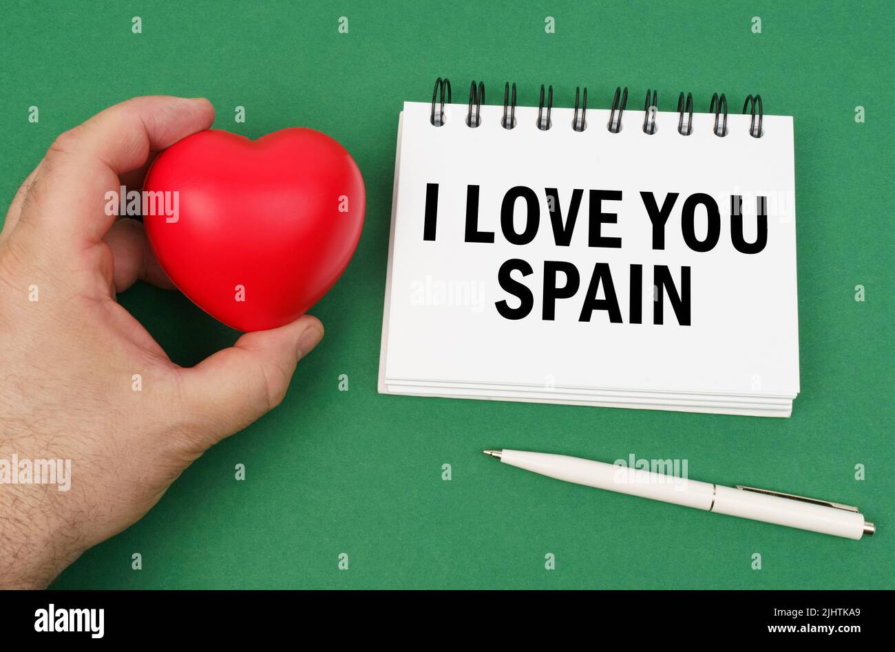 Sur la surface verte se trouvent un stylo, un bloc-notes avec l'inscription - je vous aime Espagne. Un homme a un cœur dans ses mains. Banque D'Images