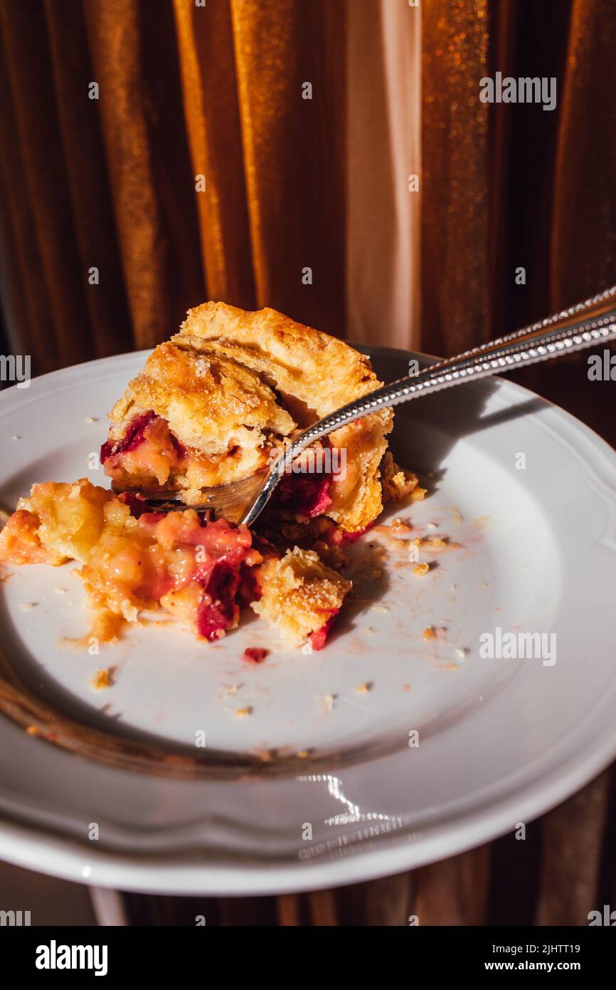 demi-tranche de tarte à la crème de rhubarbe mangée sur plaque blanche avec fourchette et fond de rideau doré Banque D'Images