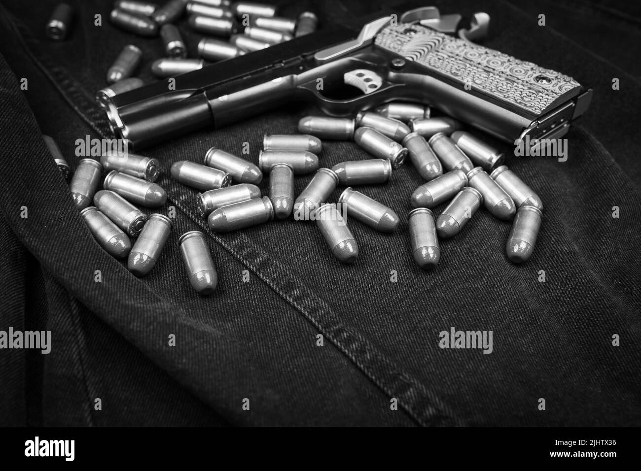 Pistolet modèle 1911 et cartouches (.45 ACP) sur fond noir denim, photo monochrome Banque D'Images