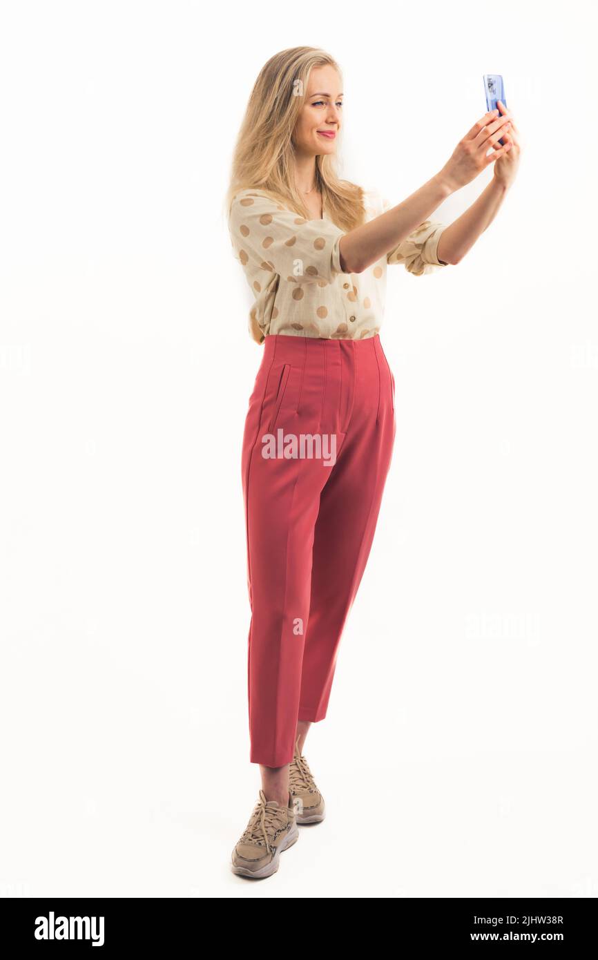 Amicale caucasienne millénaire élégante femme ouvrier de col blanc prenant un selfie avec un smartphone sur fond blanc. Prise de vue du corps entier. Photo de haute qualité Banque D'Images