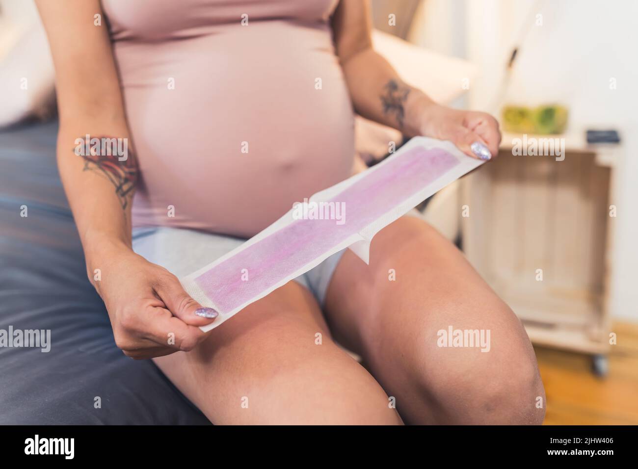 Femme enceinte de race blanche qui se dépilation pour ses jambes avec cirage, gros plan à l'intérieur. Photo de haute qualité Banque D'Images