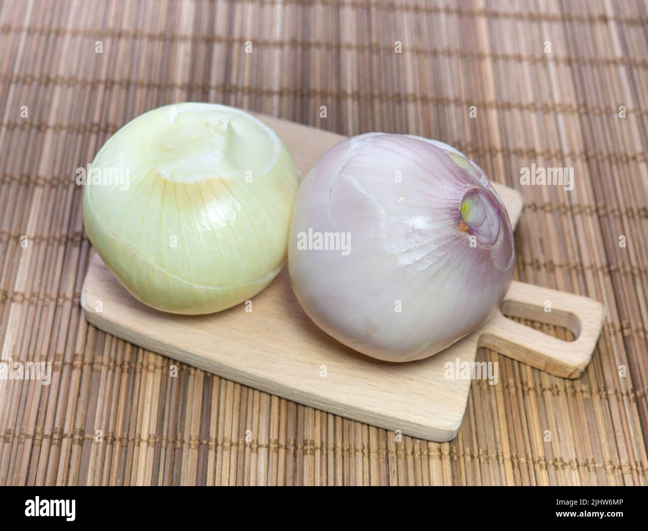 Deux oignons pelés sur une petite planche à découper. Raciner la récolte avant de cuisiner le dîner. Légumes épicés. Produit utile. Cuisine du jardin Banque D'Images