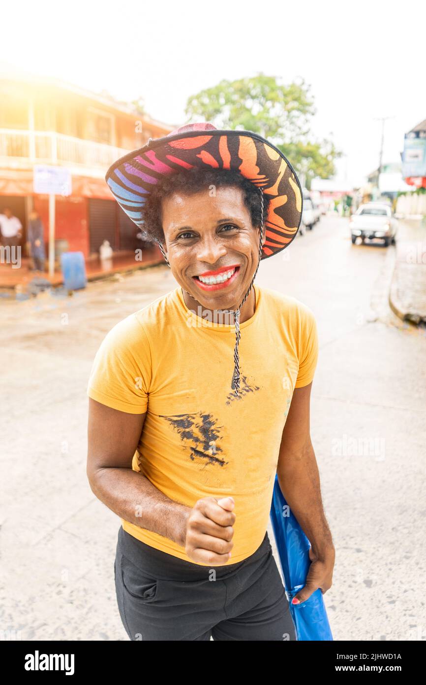 Photo verticale d'un homme latin gay à la peau noire avec chapeau coloré souriant et regardant l'appareil photo Banque D'Images