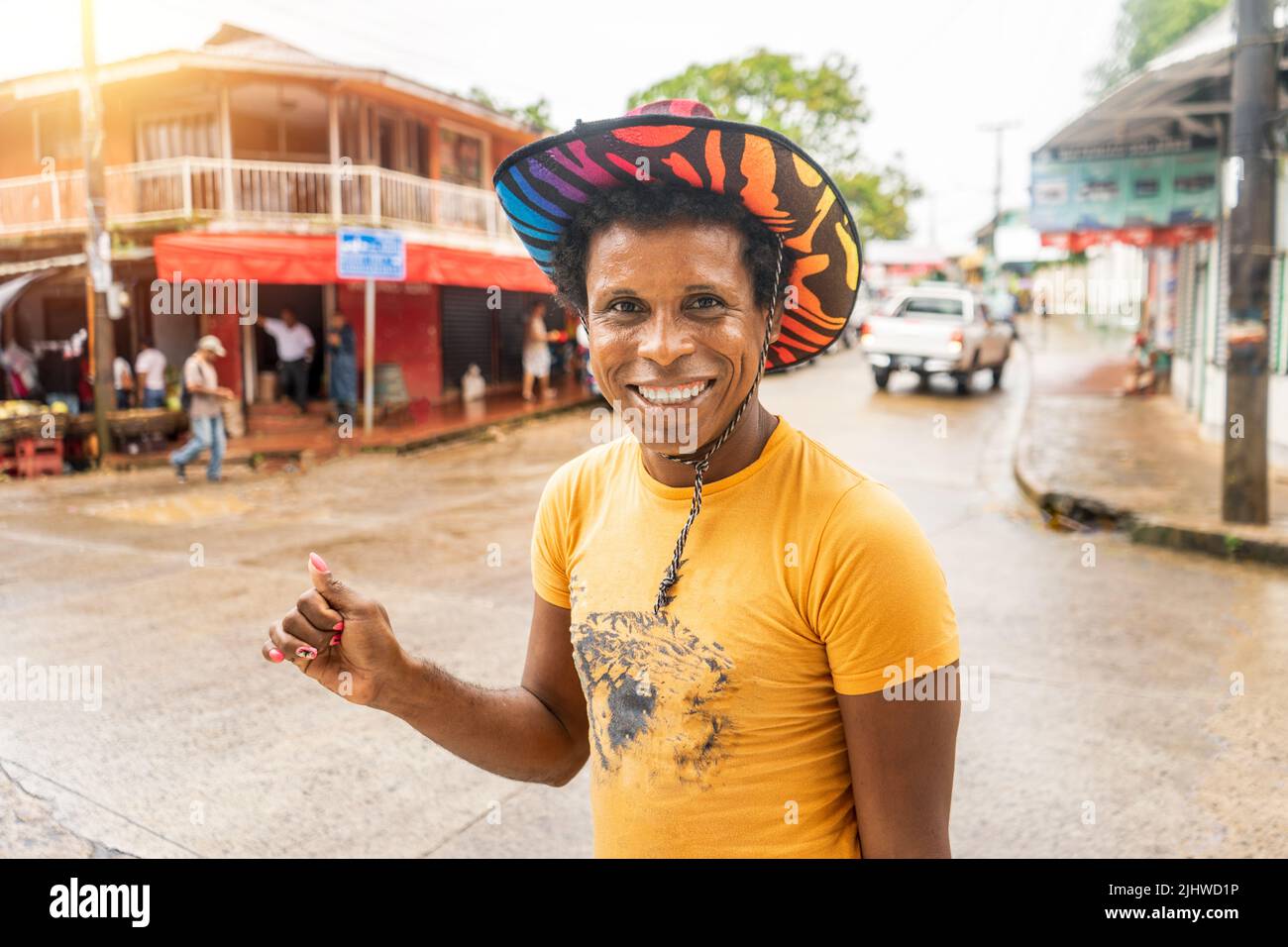latino gay à la peau noire avec chapeau coloré souriant et regardant l'appareil photo Banque D'Images