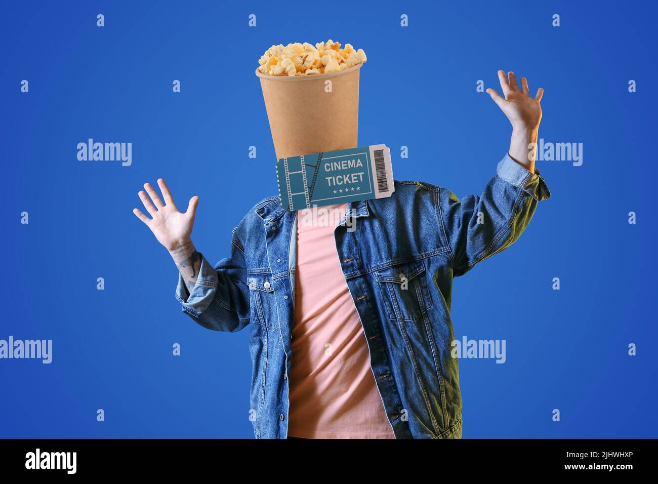 Jeune homme heureux avec un seau de maïs pop croquant au lieu de sa tête et billet de cinéma sur fond bleu Banque D'Images