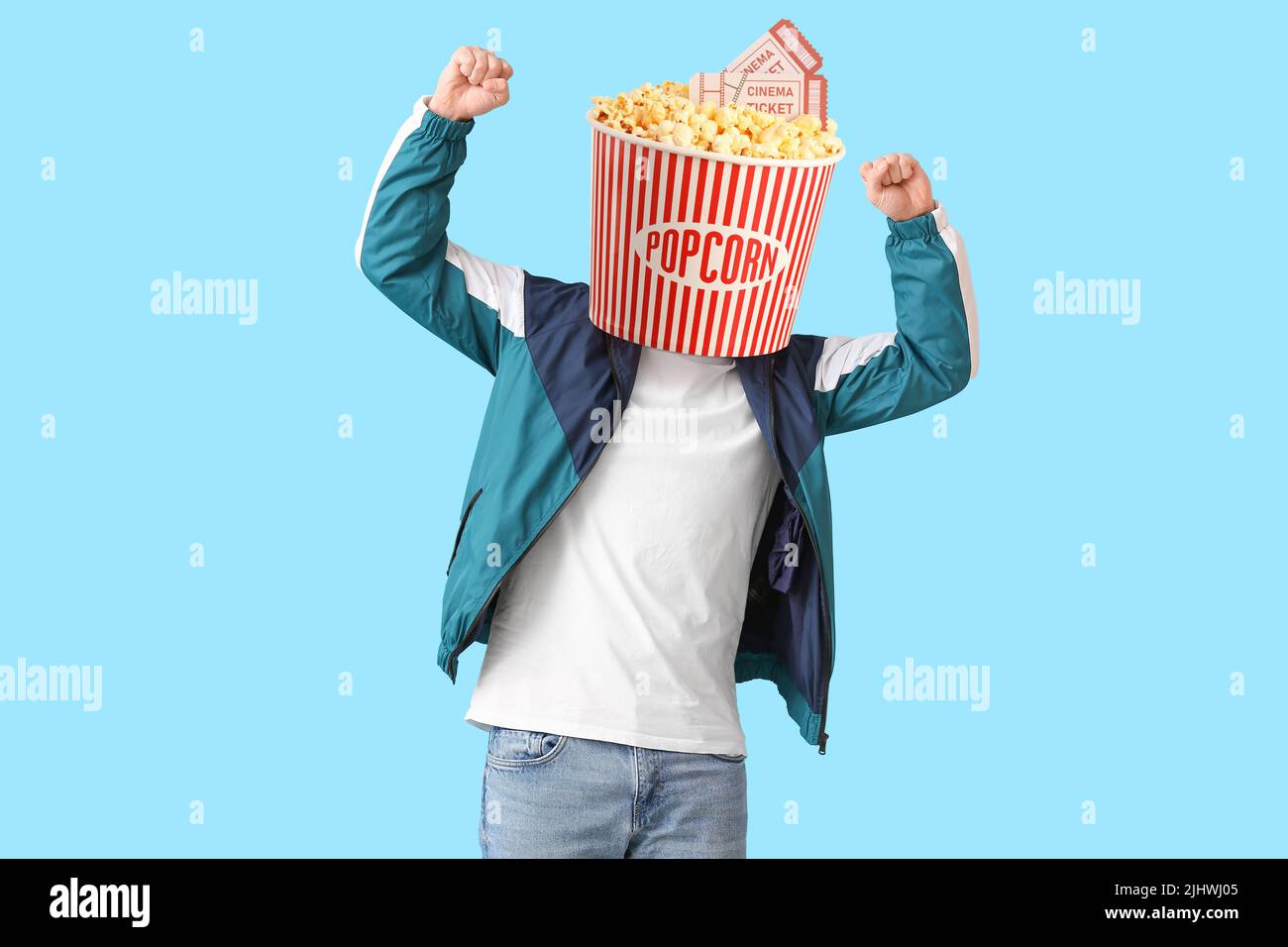 Jeune homme heureux avec un seau de maïs pop croquant au lieu de sa tête et des billets de cinéma sur fond bleu Banque D'Images