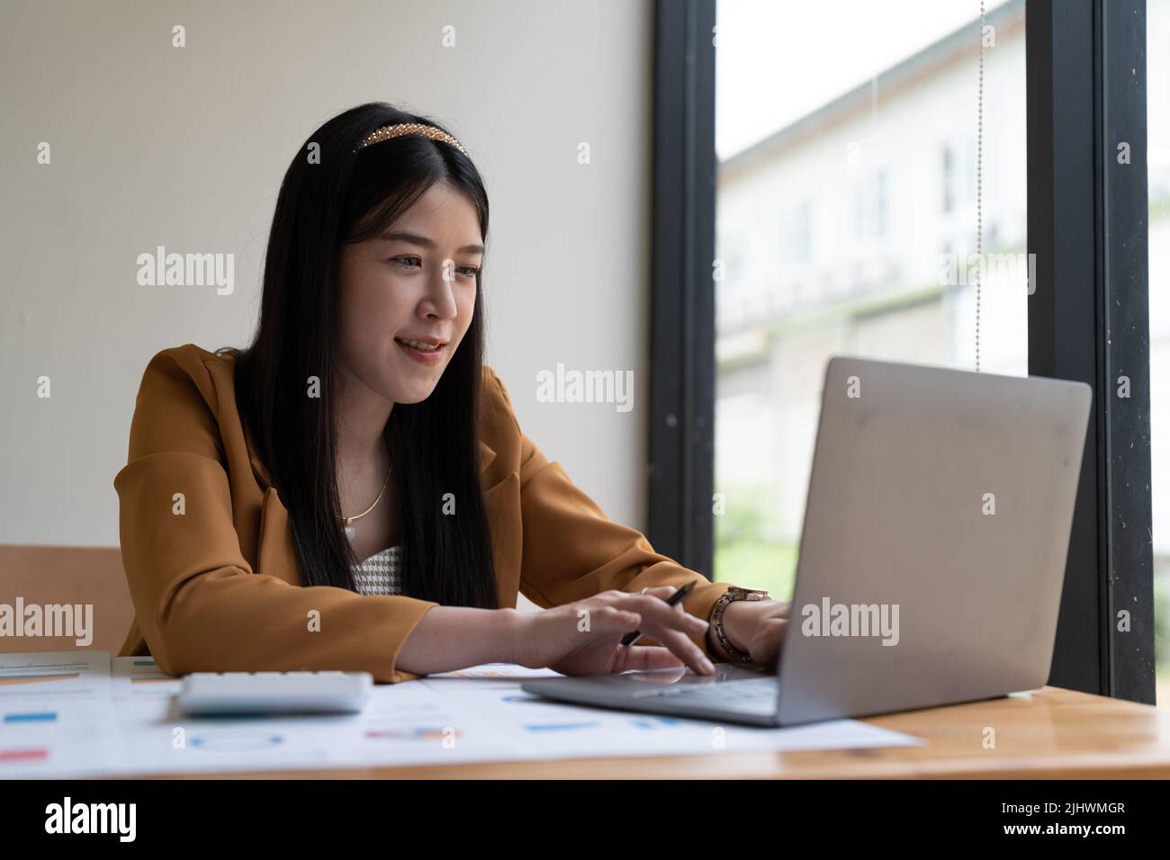 Belle jeune femme d'affaires asiatique souriante travaillant sur un ordinateur portable et buvant du café, femme d'affaires asiatique travaillant le financement de documents et la calculatrice dans elle Banque D'Images