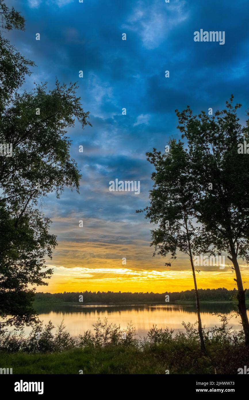 un beau lac bleu avec quelques silhouettes d'arbres au premier plan sous un ciel spectaculaire de coucher de soleil.Photo de haute qualité Banque D'Images
