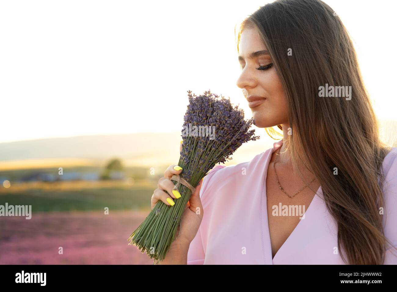 Jeune femme en robe tenant un bouquet de fleurs debout dans le champ de lavande Banque D'Images